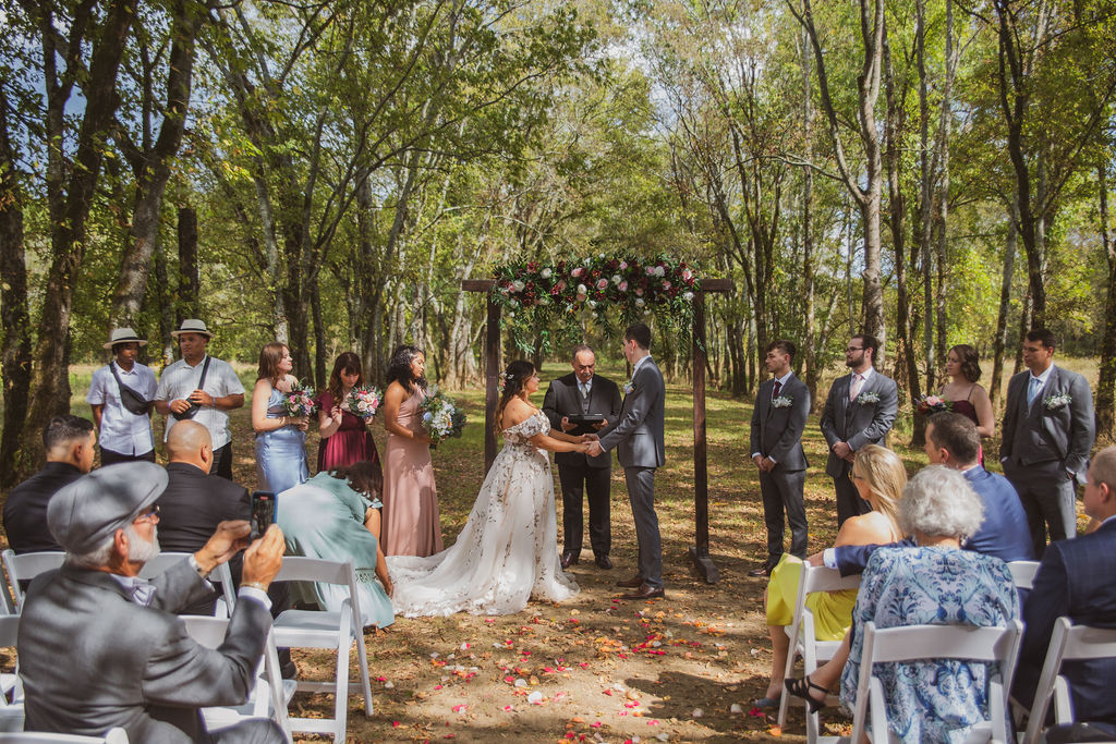 Jen & Alec exchange vows under a floral wooden arbor along the Tunnel of Love at Covey Creek