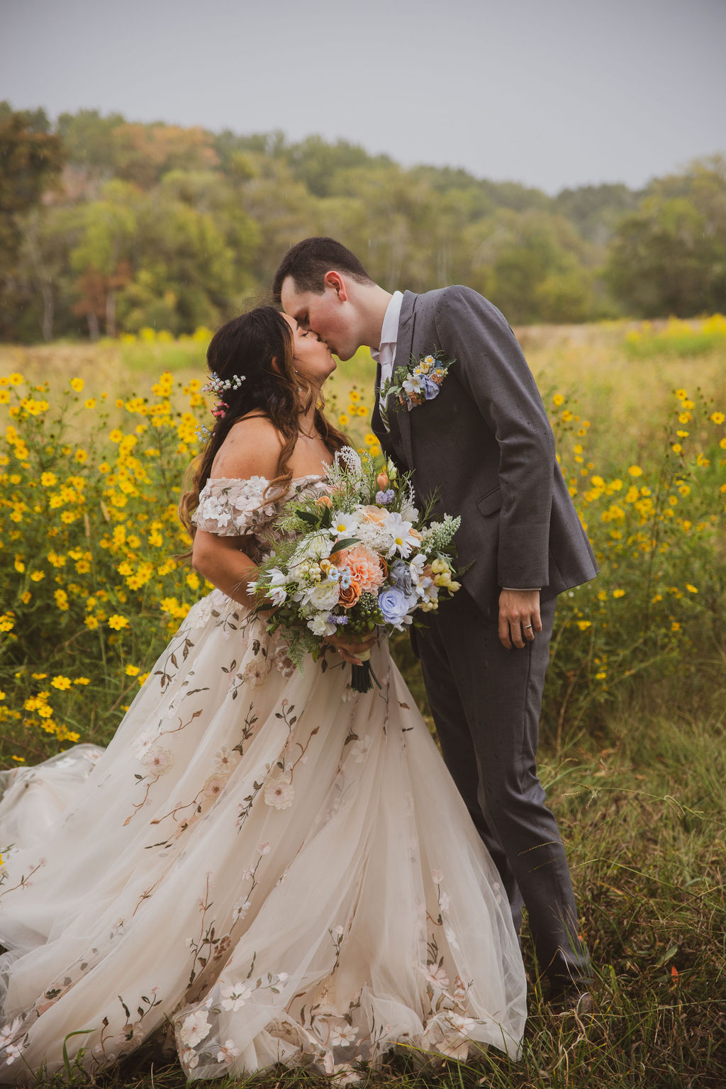Jen & Alec kiss amid tall yellow wildflowers under misty trees in floral gown at Covey Creek