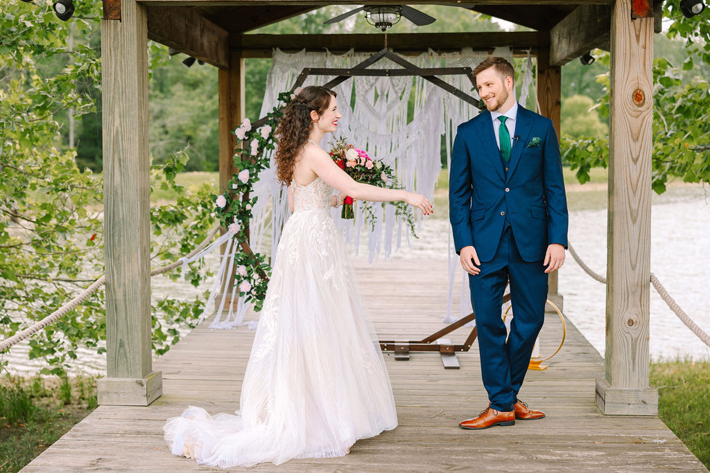 Kate & Josh stand on Covey Creek’s Pond dock under a macrame hexagonal arch with pink roses
