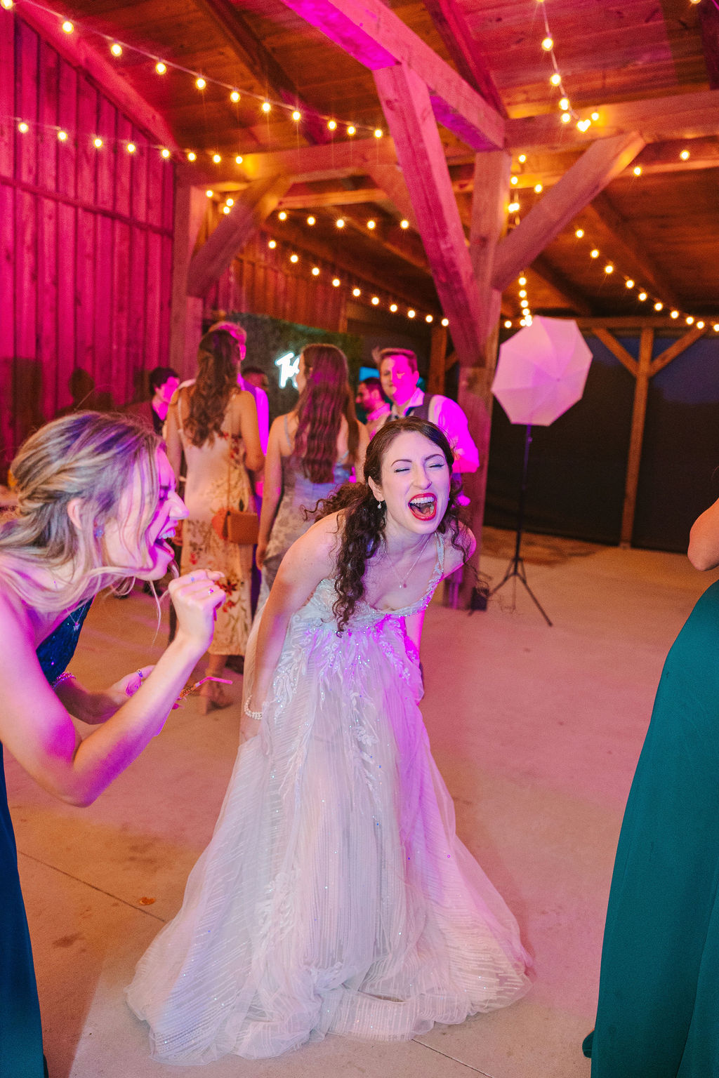 Kate & Josh reception: Kate laughs mid-dance in the Covey Creek barn under pink lights and Edison bulbs
