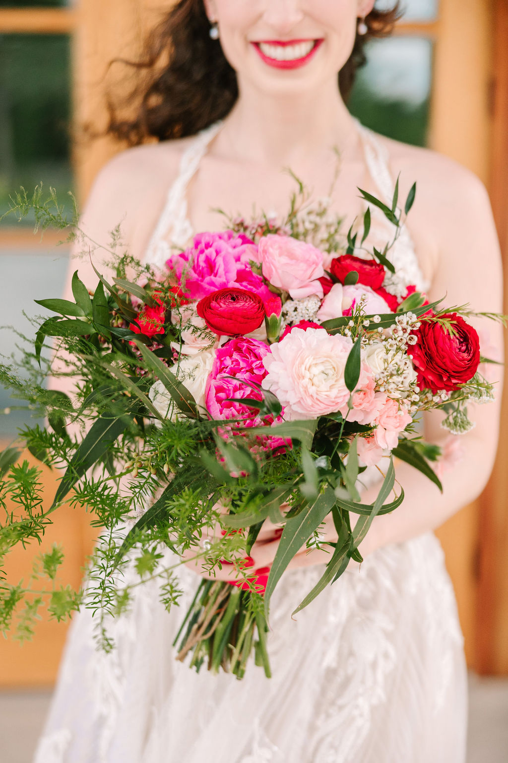 Kate of Kate & Josh smiles with her pink-red rose bouquet at Covey Creek, lace gown in frame