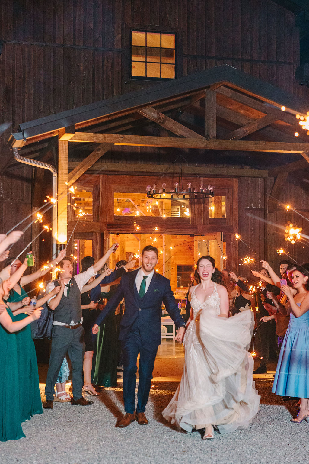 Kate & Josh run through a sparkler tunnel outside Covey Creek’s barn, laughing toward the camera