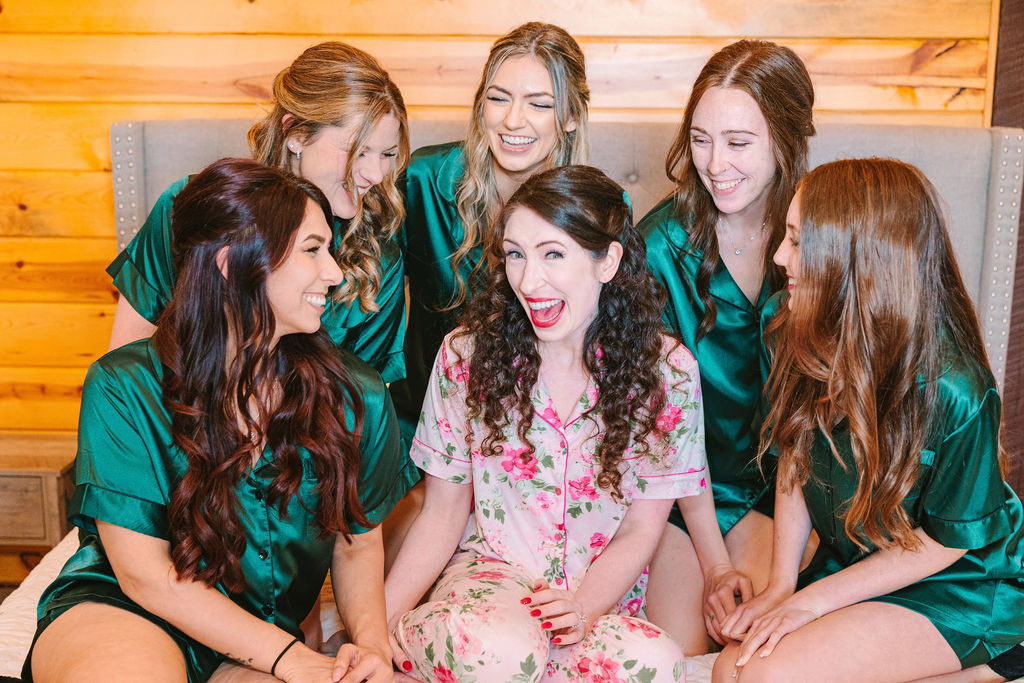 Kate of Kate & Josh and bridesmaids in emerald pajamas laugh together in Covey Creek’s bridal suite