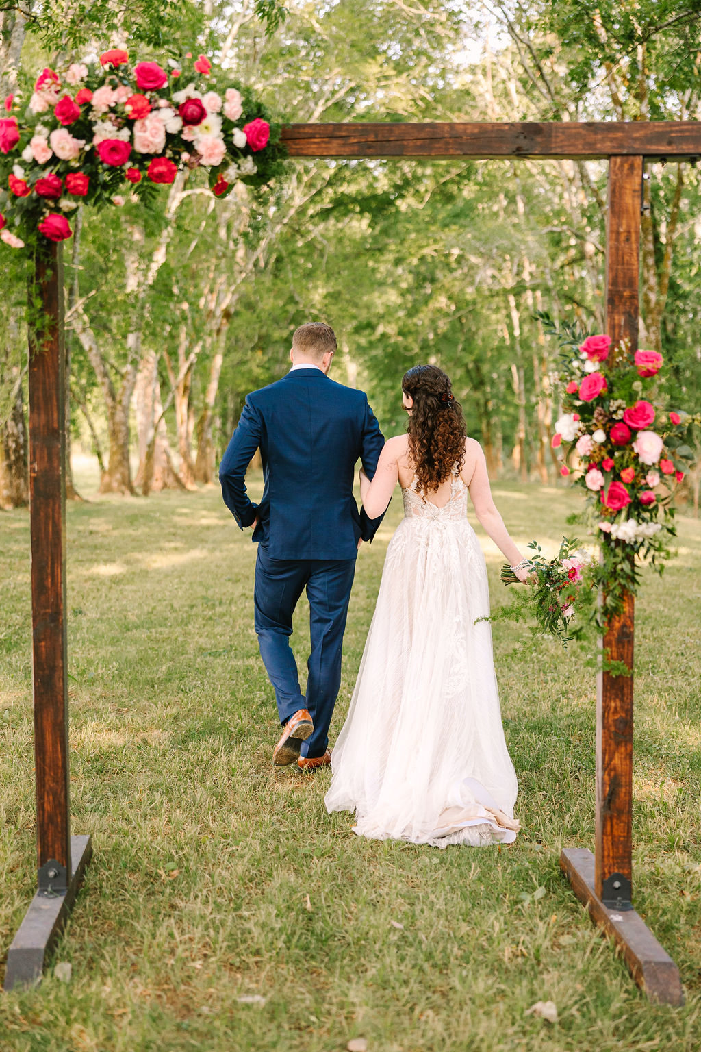 Kate & Josh walk arm-in-arm away through Covey Creek’s floral ceremony arch toward the tree line