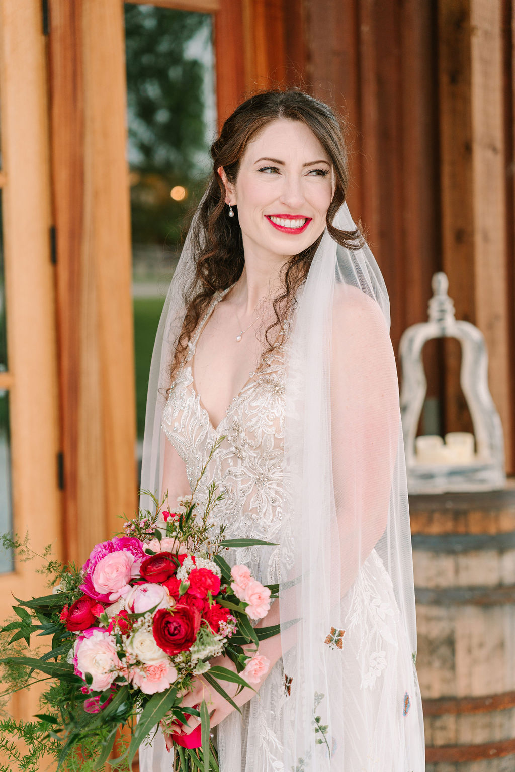 Kate of Kate & Josh smiles in lace gown and veil at Covey Creek, holding a pink and red rose bouquet