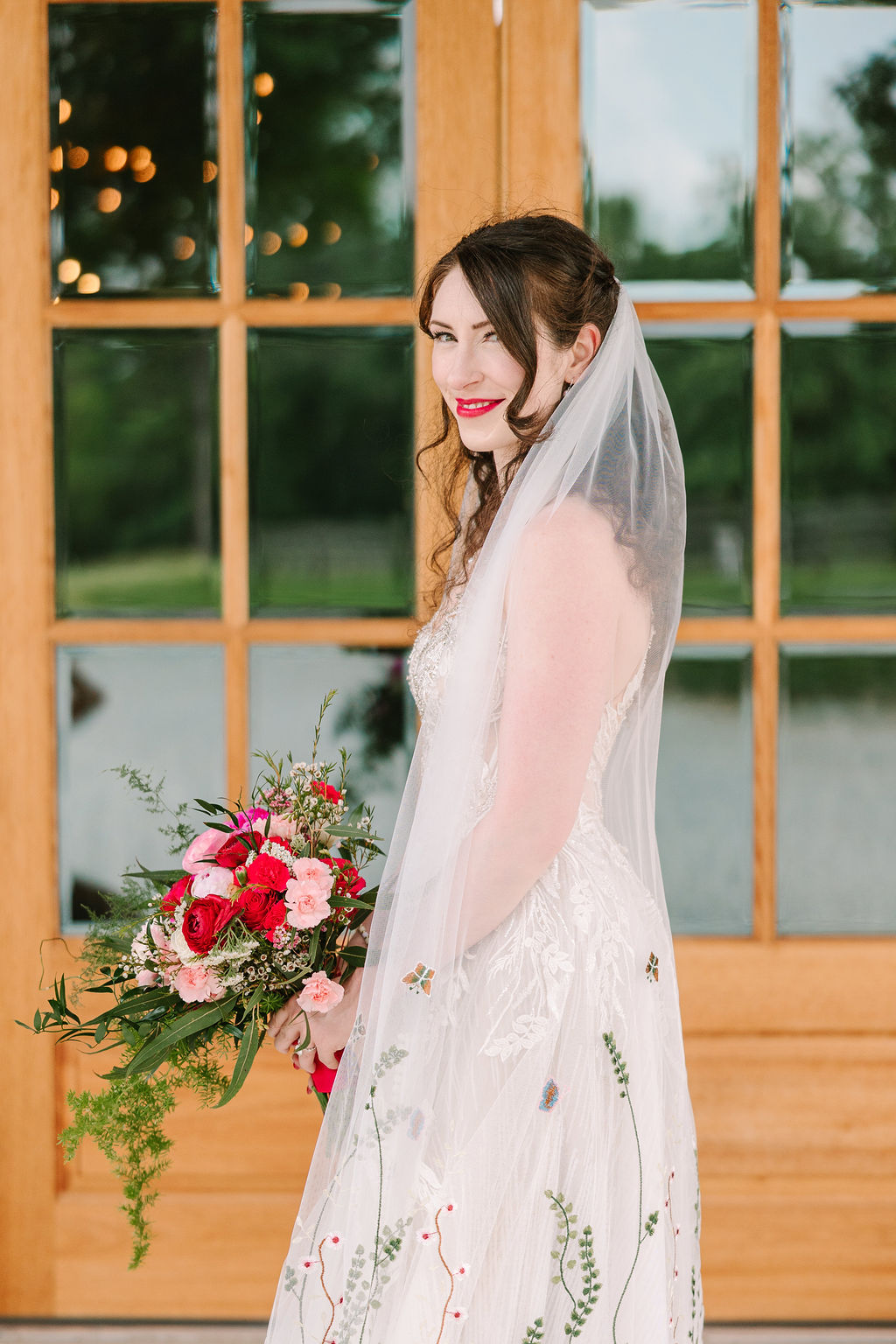 Bride Kate of Kate & Josh smiles over her shoulder at Covey Creek in a floral-embroidered gown and veil