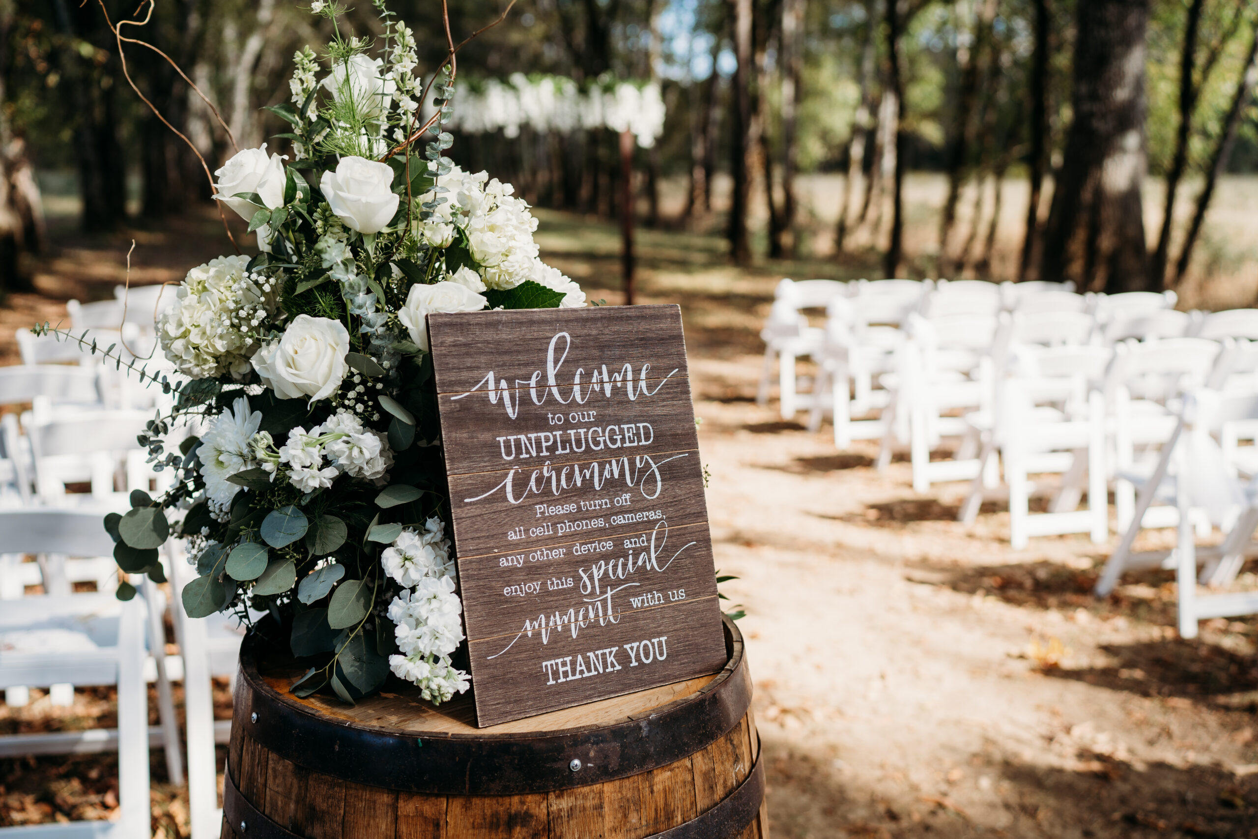 Unplugged ceremony sign and white rose barrel arrangement for Levi & Billy at Covey Creek woods
