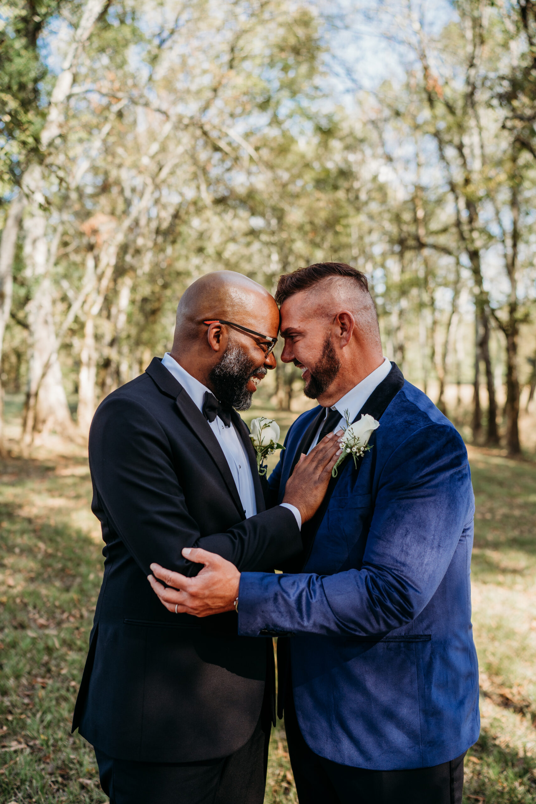 Levi & Billy press foreheads together in black tuxedo and cobalt velvet blazer at Covey Creek woods