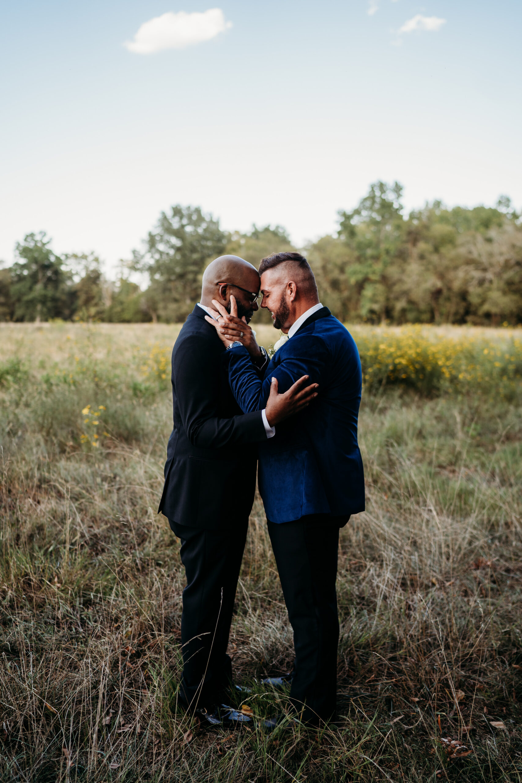 Levi & Billy press foreheads in tall wildflower grass, blue velvet and black suit at Covey Creek