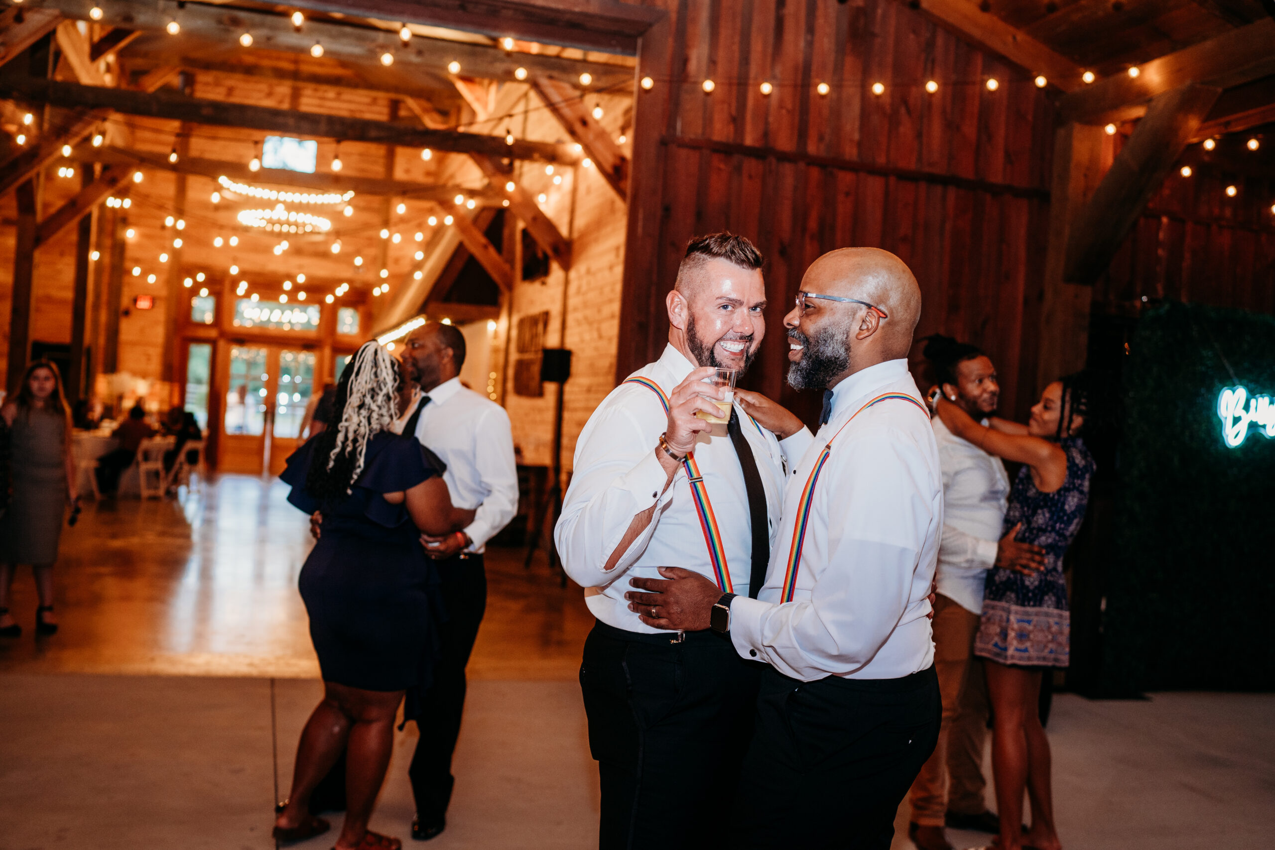 Levi & Billy slow dance in matching rainbow suspenders under barn string lights at Covey Creek