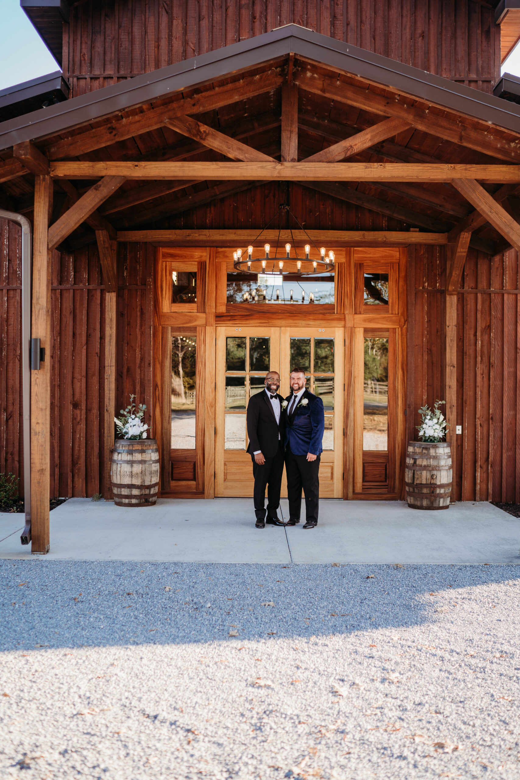 Levi & Billy pose at Covey Creek barn doors under Edison chandelier flanked by flower barrels
