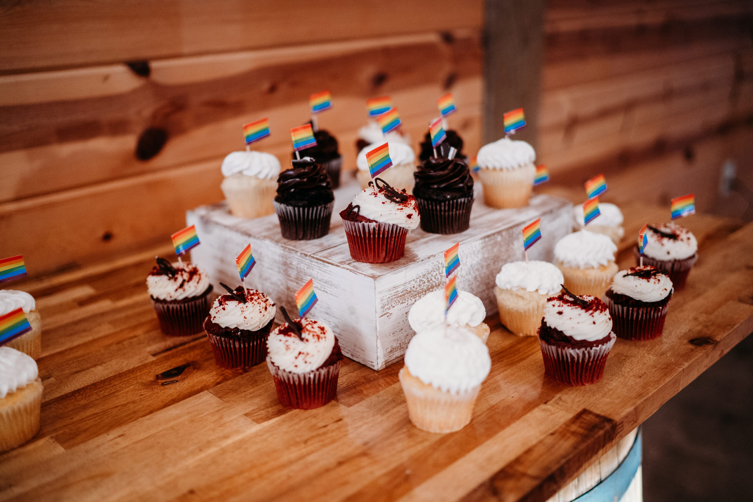 Rainbow-flag cupcakes on a rustic wood riser for Levi & Billy’s reception dessert at Covey Creek