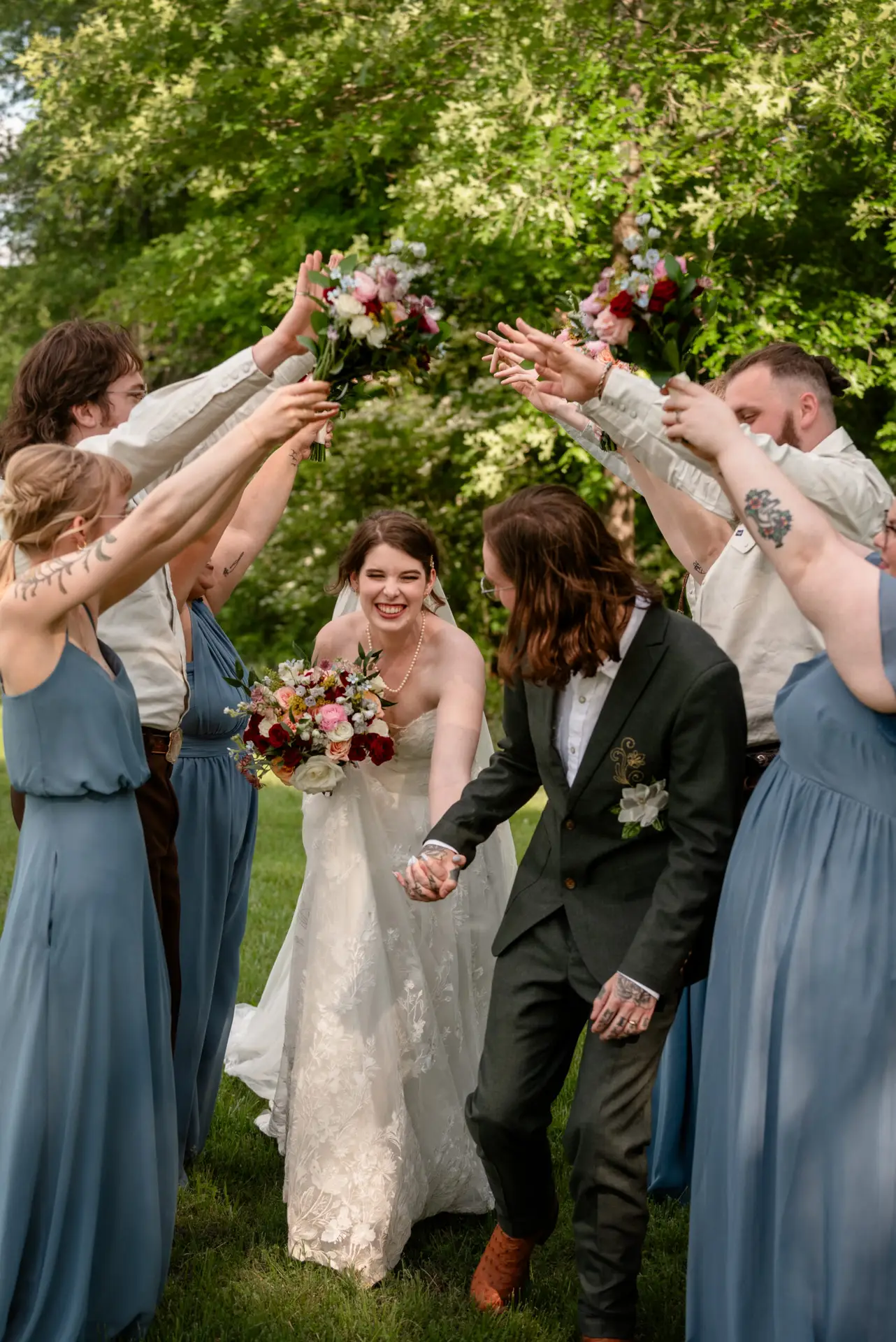 Rachael & Ben walk laughing under a wedding-party arch on the green lawn outdoors at Covey Creek.