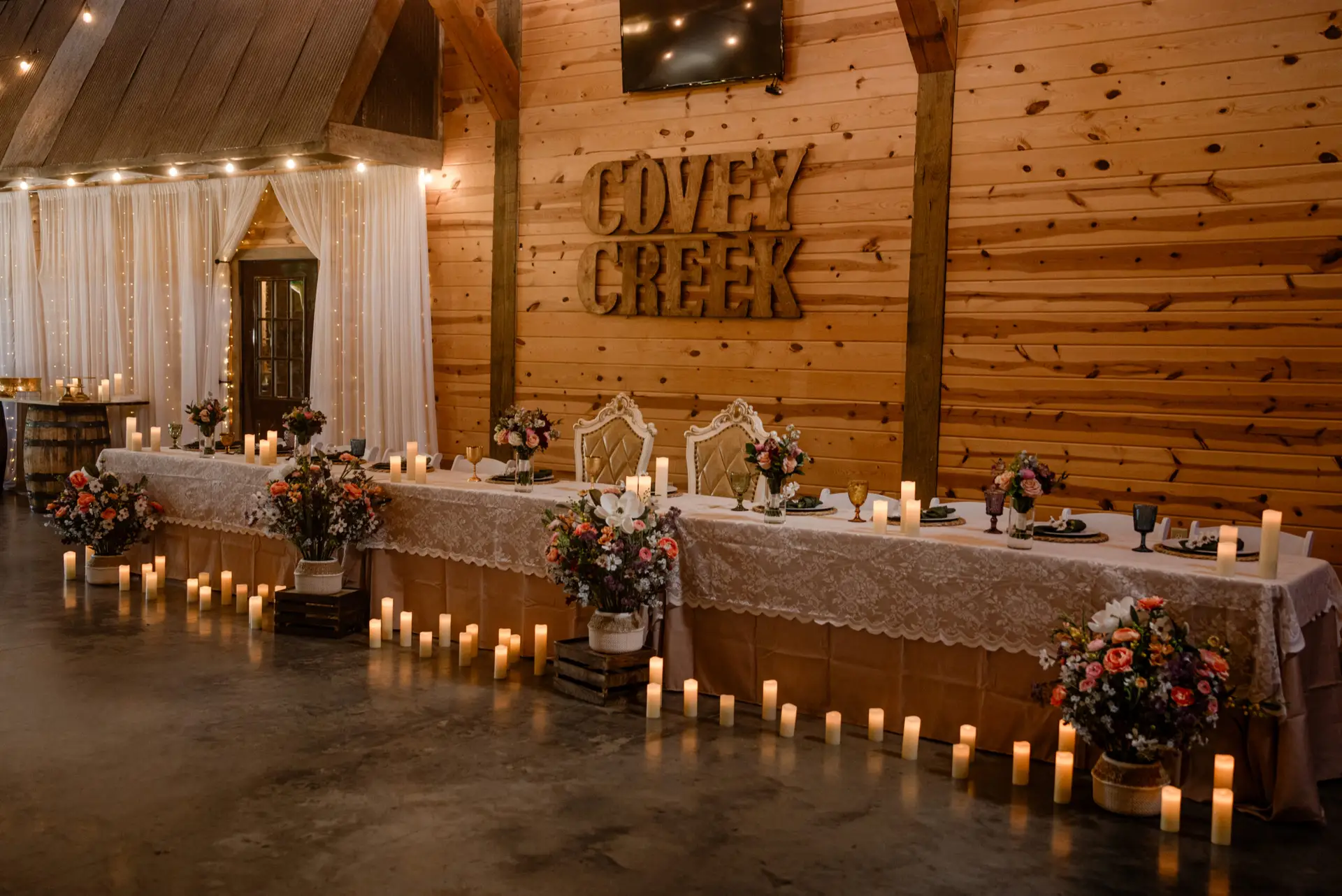 Indoor head table with Covey Creek wood sign, pillar candles, and florals for Rachael & Ben at Covey Creek.