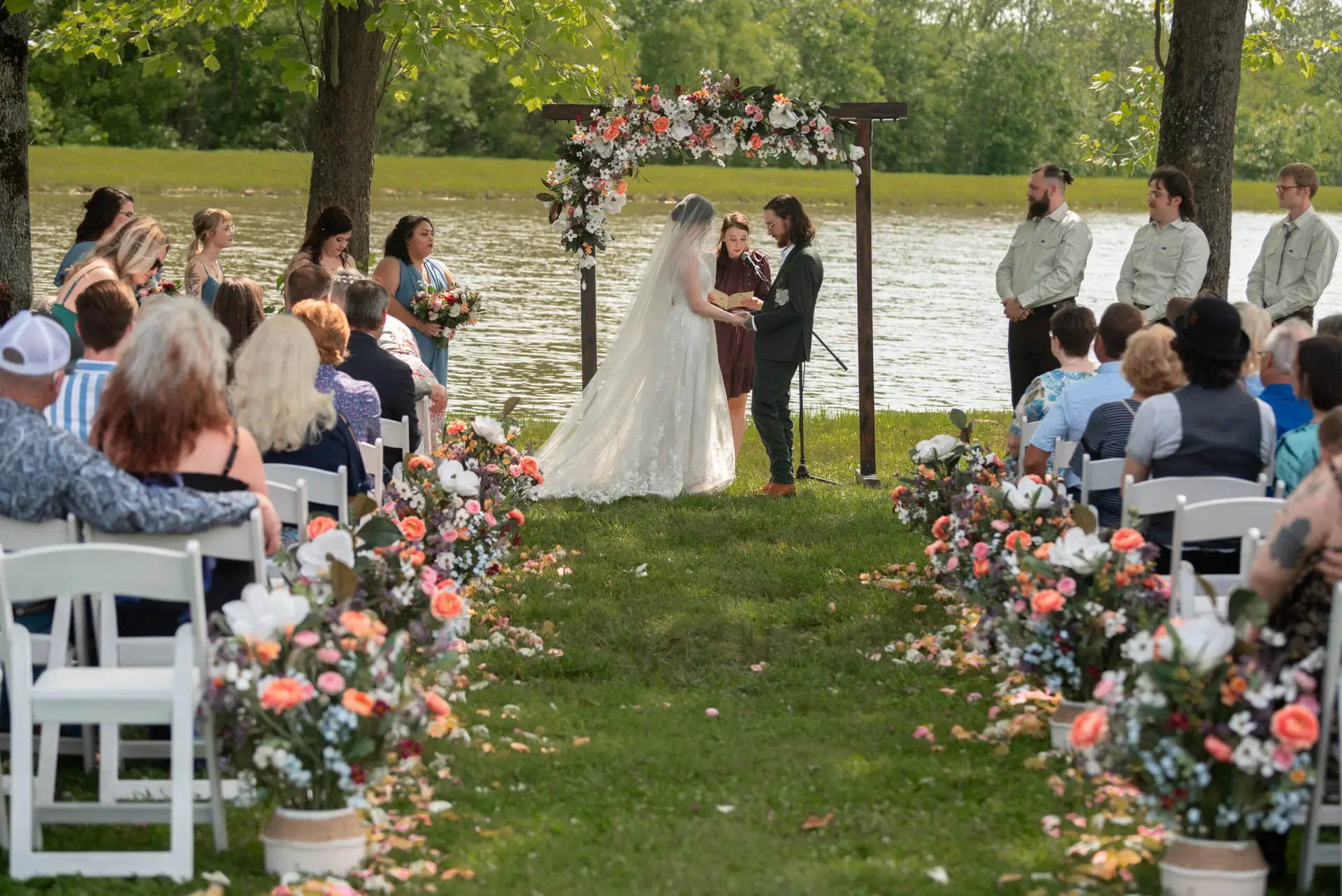 Guests watch Rachael & Ben exchange vows at the floral pond arbor ceremony at Covey Creek.