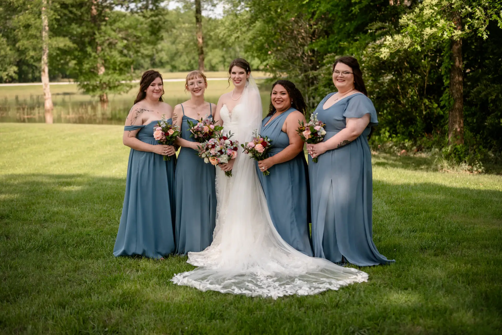Rachael with bridesmaids in dusty blue pose on the lawn by the pond at Covey Creek, Rachael & Ben.