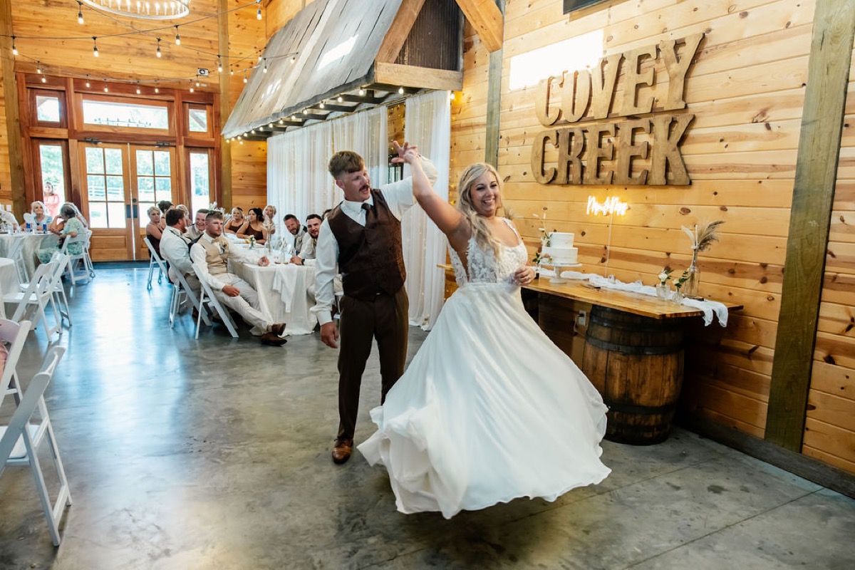 Alexis & Logan twirl by their cake under the Covey Creek wall letters indoors at Covey Creek