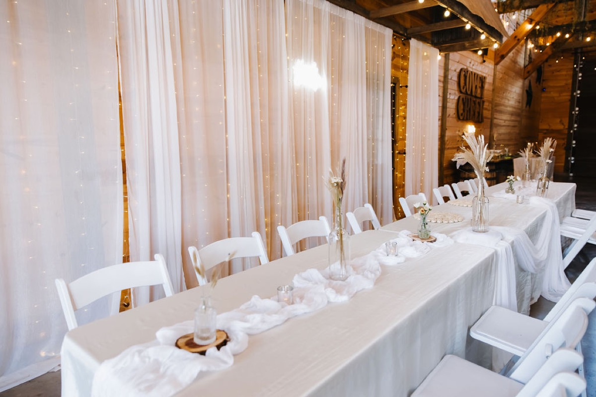 Alexis & Logan long banquet table with sheer light backdrop beside the Covey Creek wall sign indoors