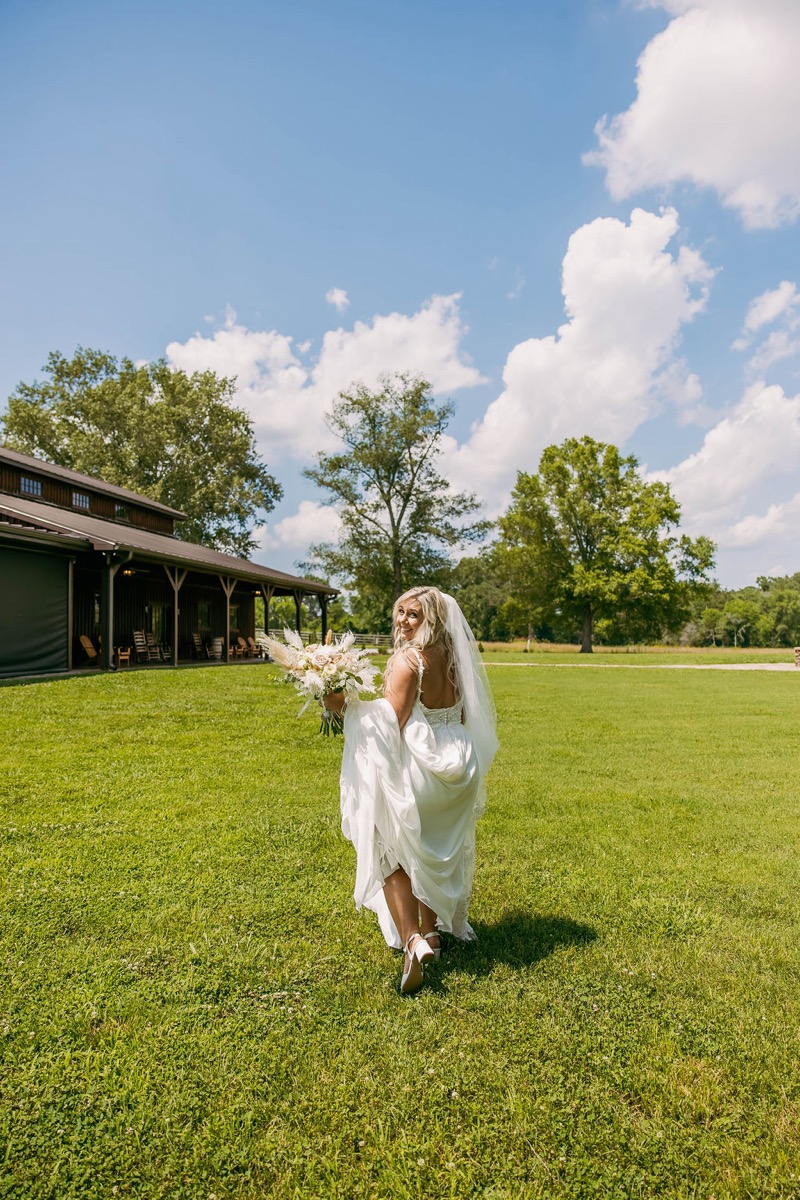 Alexis & Logan: Alexis looks back over her shoulder on the lawn with the barn behind at Covey Creek