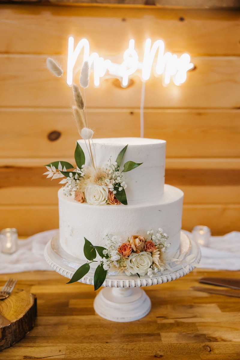 Alexis & Logan two-tier white cake with peach roses and pampas under a Mr. & Mrs. neon at Covey Creek