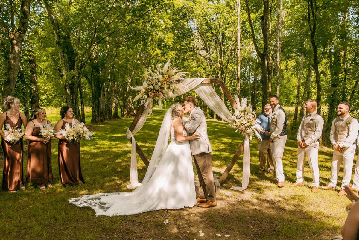 Alexis & Logan kiss under the floral hexagonal arch with bridal party at Covey Creek Tunnel of Love