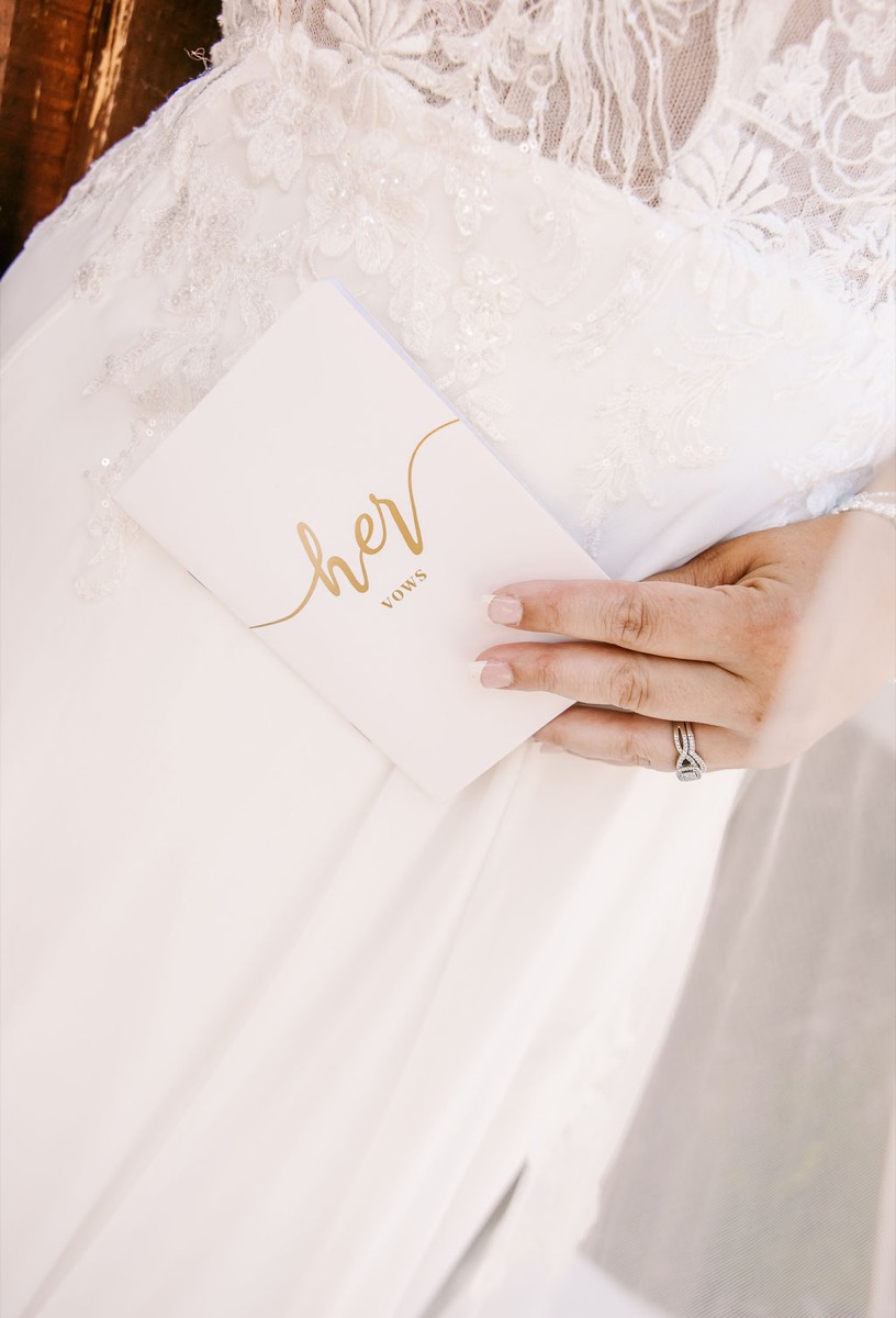 Alexis & Logan: Alexis holds her vows booklet against lace gown, diamond rings in close-up at Covey Creek