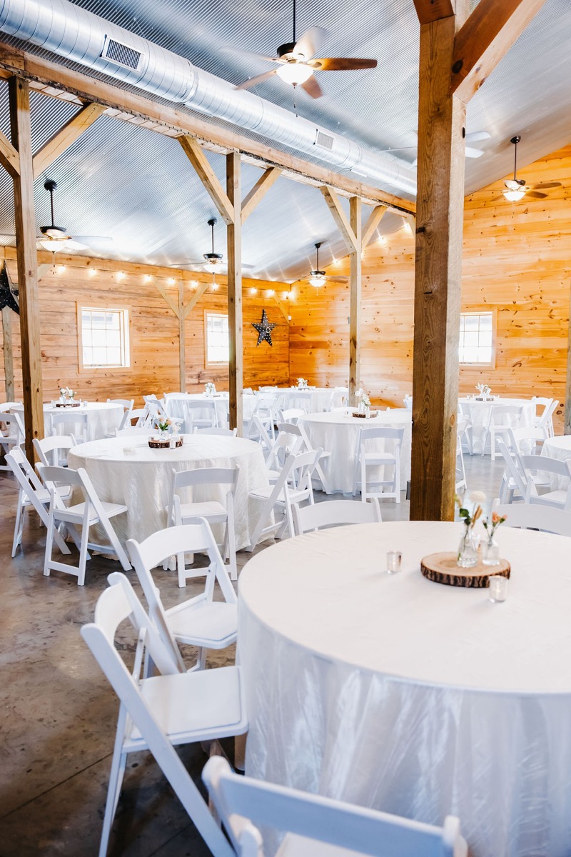 Alexis & Logan barn reception hall with round white tables, wood-slice centerpieces, and lights at Covey Creek