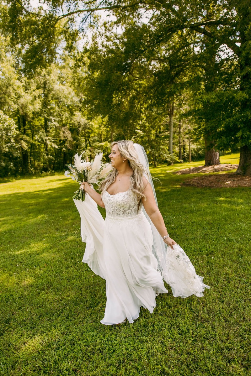 Alexis & Logan: Alexis walks laughing on the lawn in a lace gown, veil, and pampas bouquet at Covey Creek