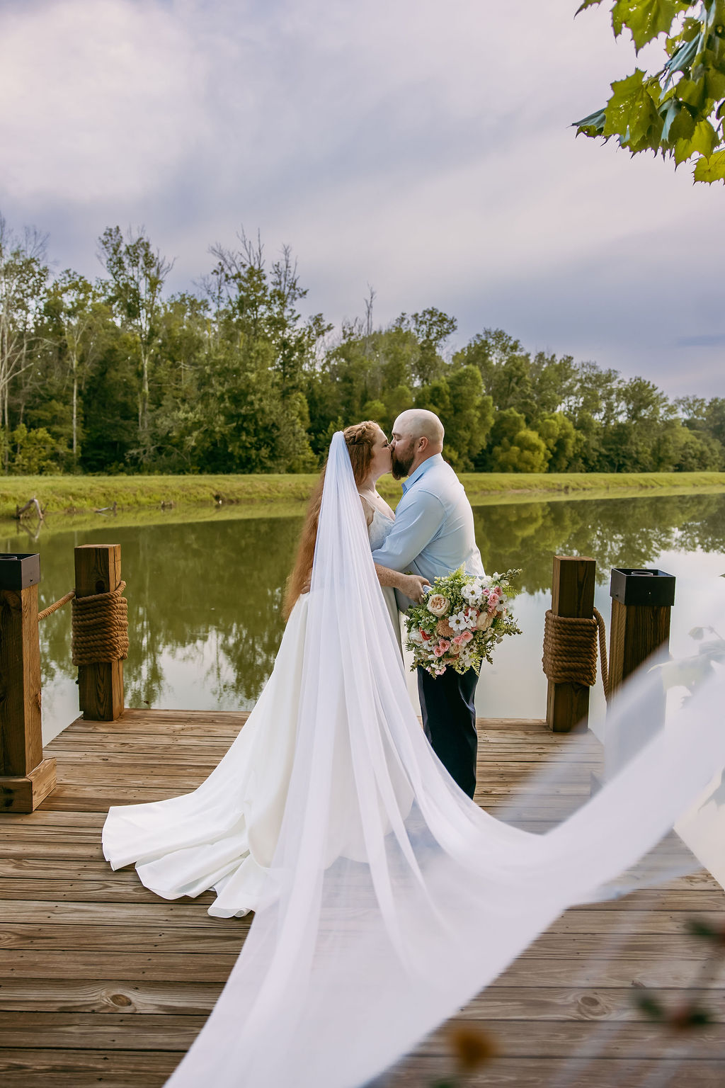 Amanda & Stephen kiss on Covey Creek’s Pond dock, her long veil trailing across the wooden planks