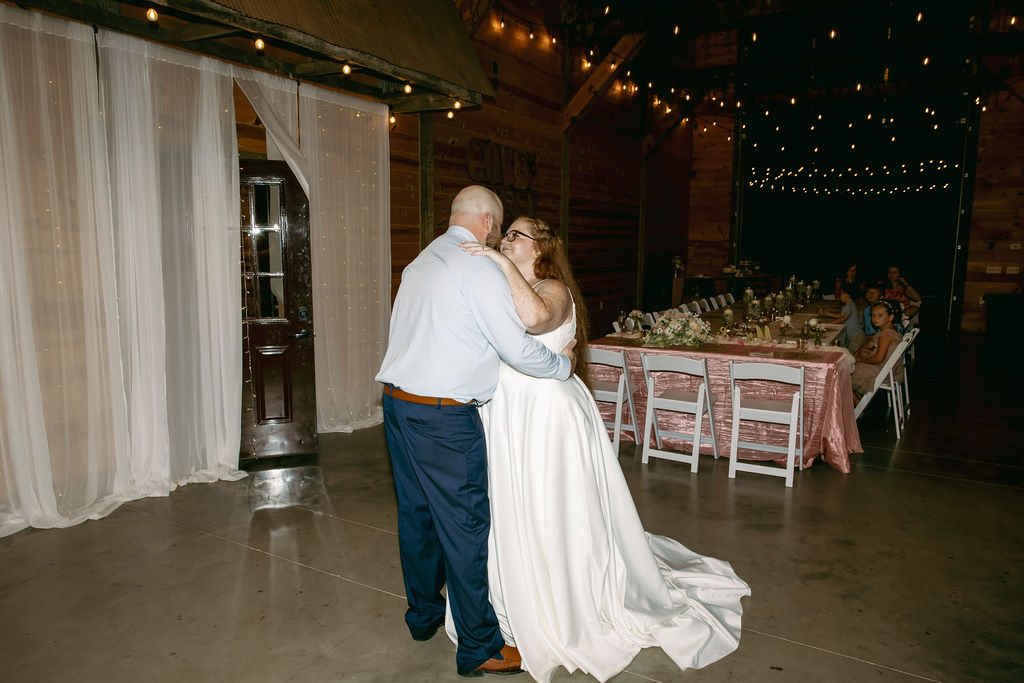 Amanda & Stephen dance indoors at Covey Creek beneath string lights, venue name painted on the wall
