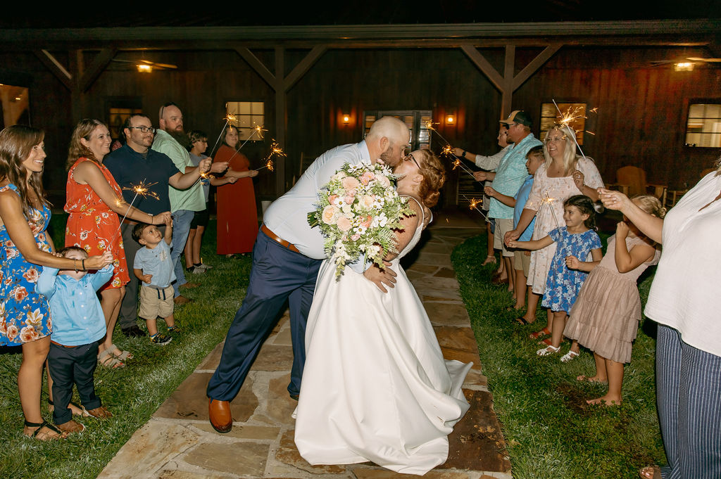 Amanda & Stephen kiss during a sparkler send-off outside Covey Creek’s barn as guests line the path
