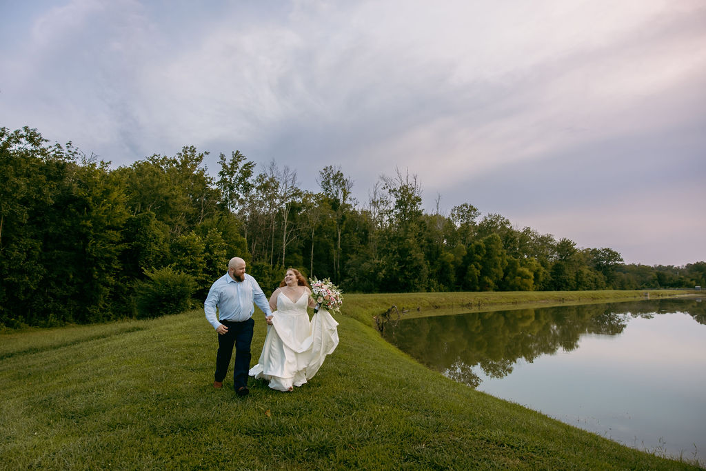 Amanda & Stephen walk hand-in-hand along Covey Creek’s Pond bank, trees reflecting in the still water