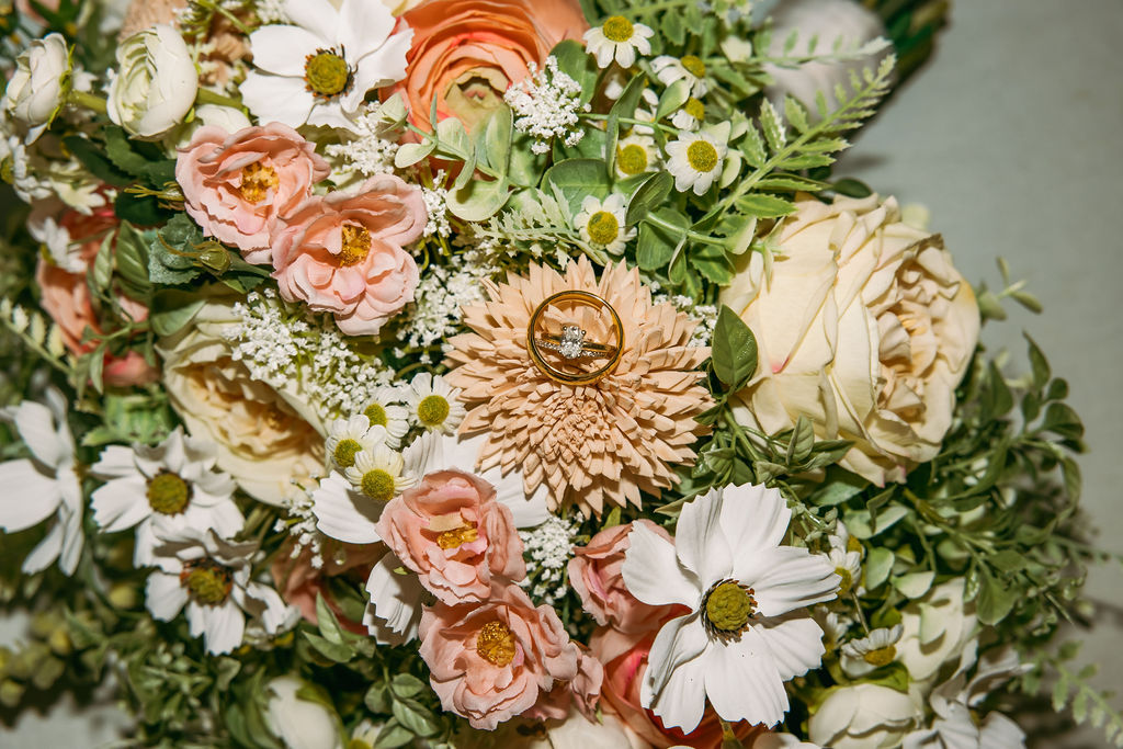 Amanda & Stephen’s gold and diamond rings nestled in a peach-and-cream floral bouquet at Covey Creek