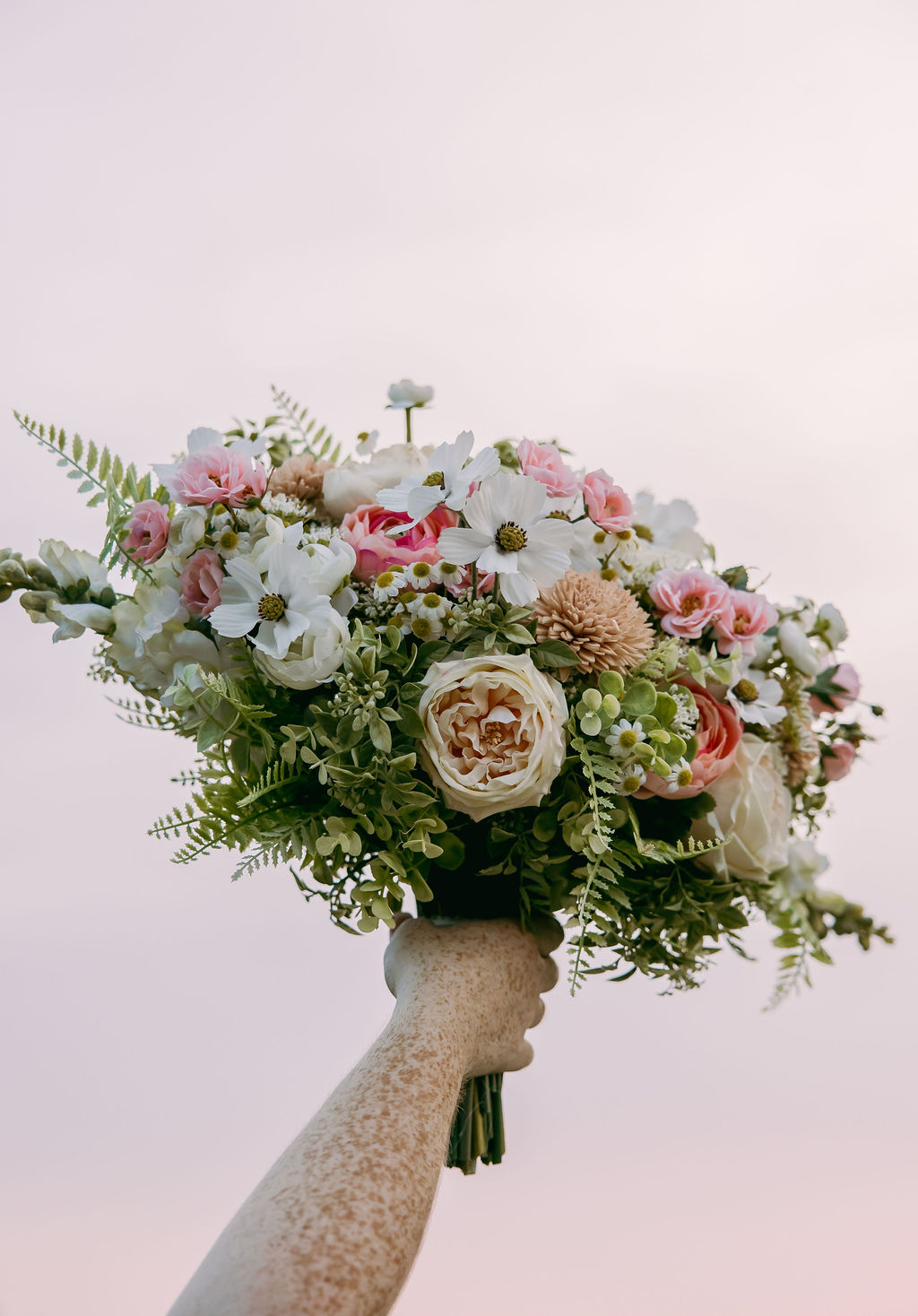 Amanda & Stephen’s garden bouquet of cream roses, cosmos, and ferns held aloft against Covey Creek sky