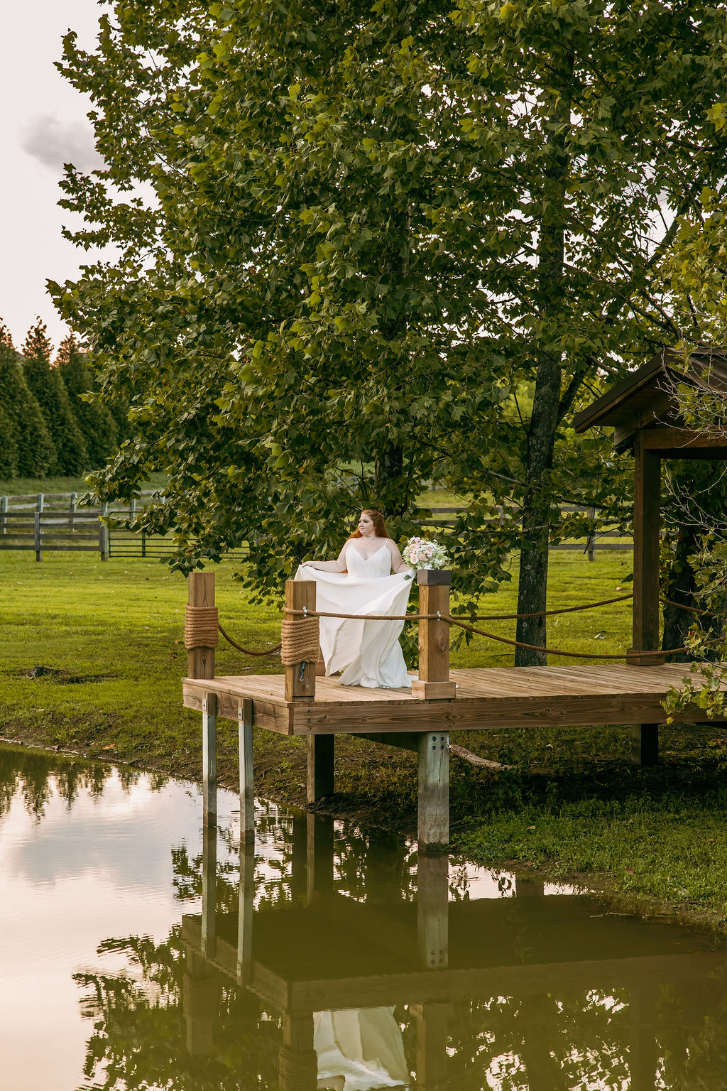 Amanda & Stephen’s bride fans her white gown on Covey Creek’s Pond dock, bouquet resting on a post