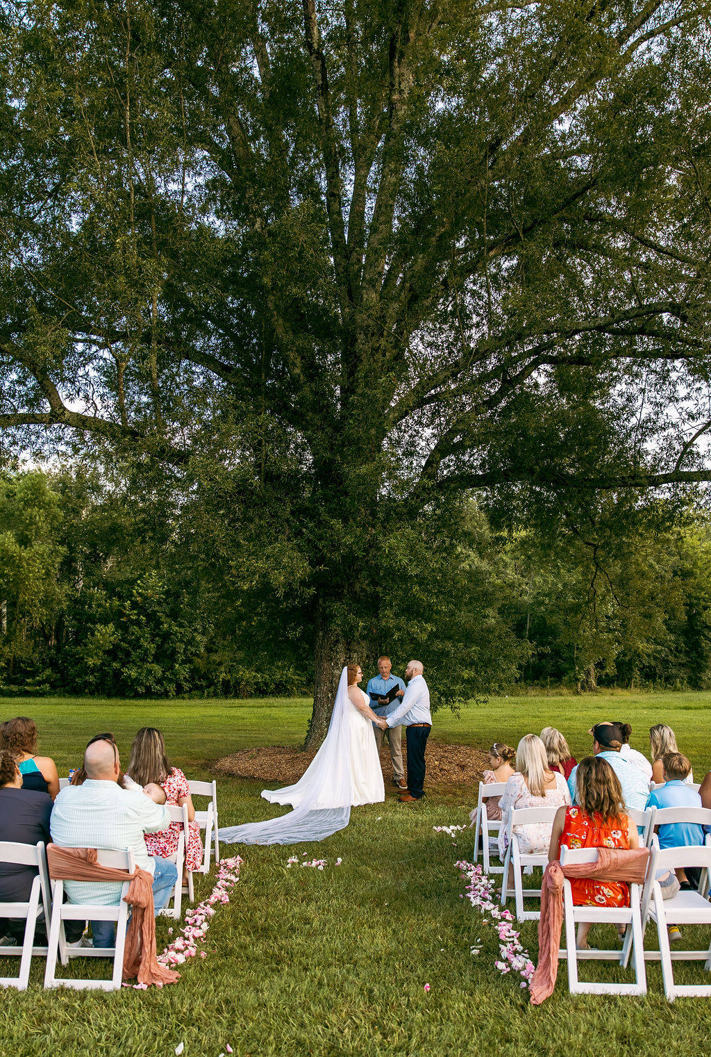 Amanda & Stephen exchange vows under Covey Creek’s Tunnel of Love oak as guests sit on white chairs