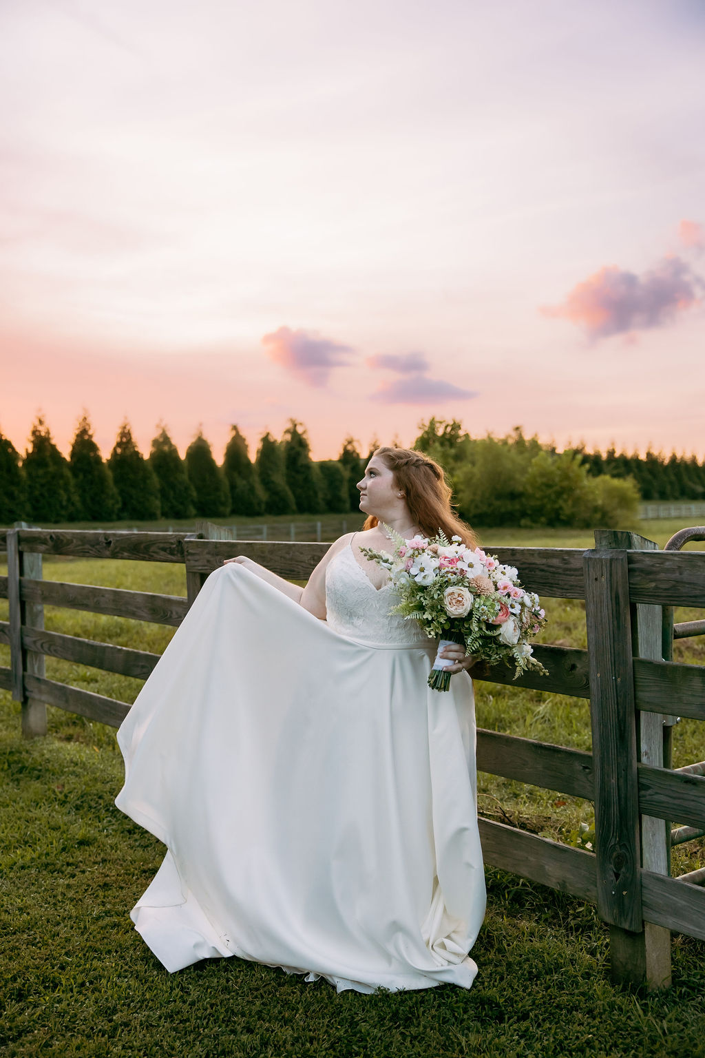 Amanda & Stephen’s bride stands by a post-and-rail fence at Covey Creek sunset, holding her bouquet