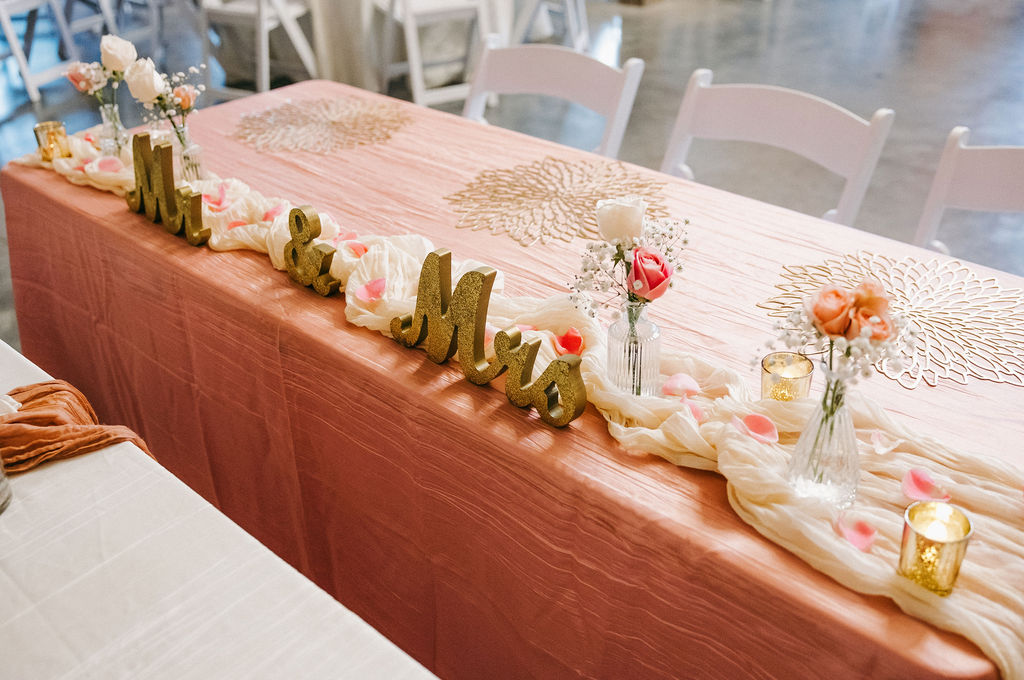 Amanda & Stephen’s peach sweetheart table at Covey Creek with gold Mr & Mrs letters, roses, and votives