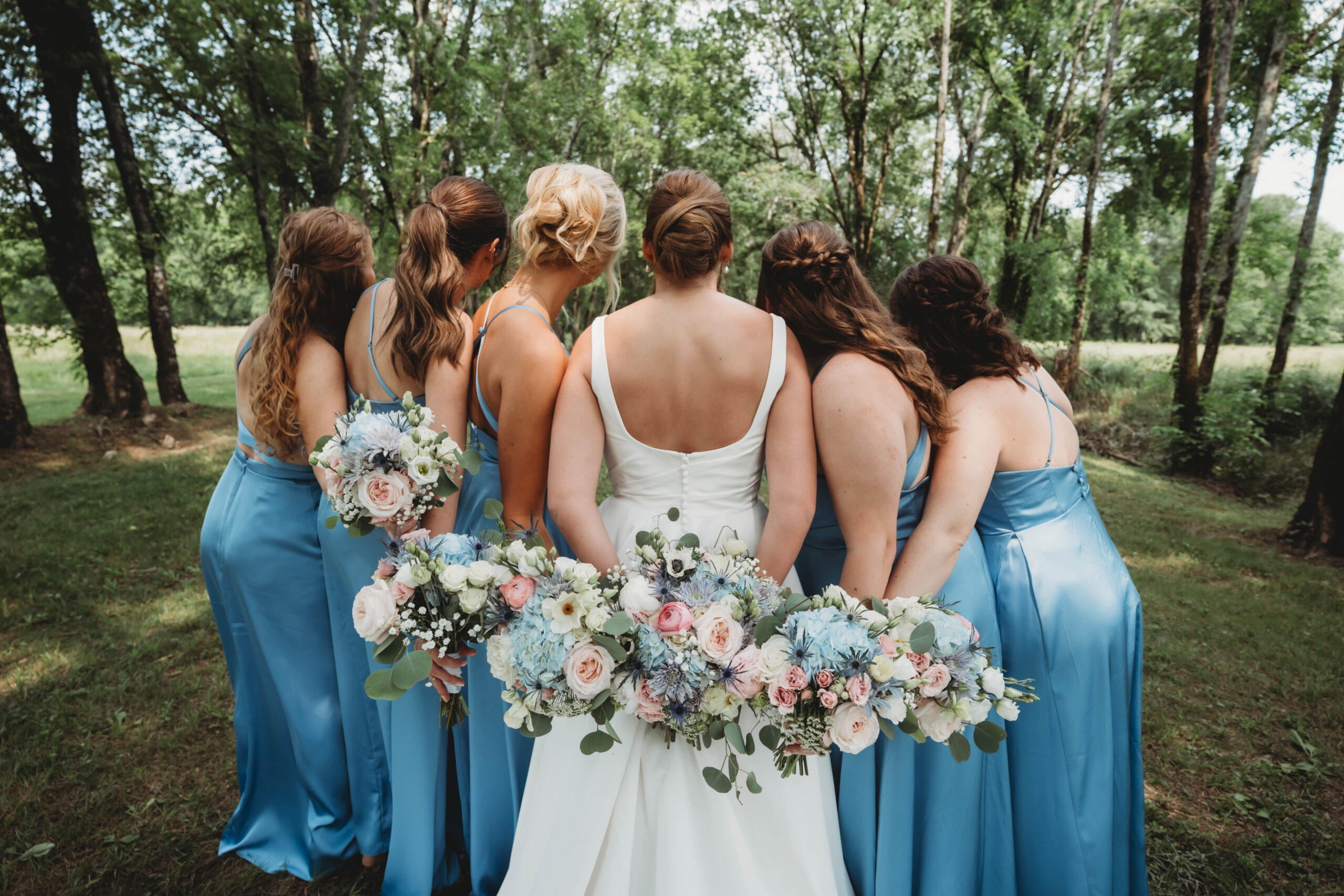Anna and bridesmaids in dusty blue hold bouquets behind their backs for Anna & Jaden at Covey Creek.