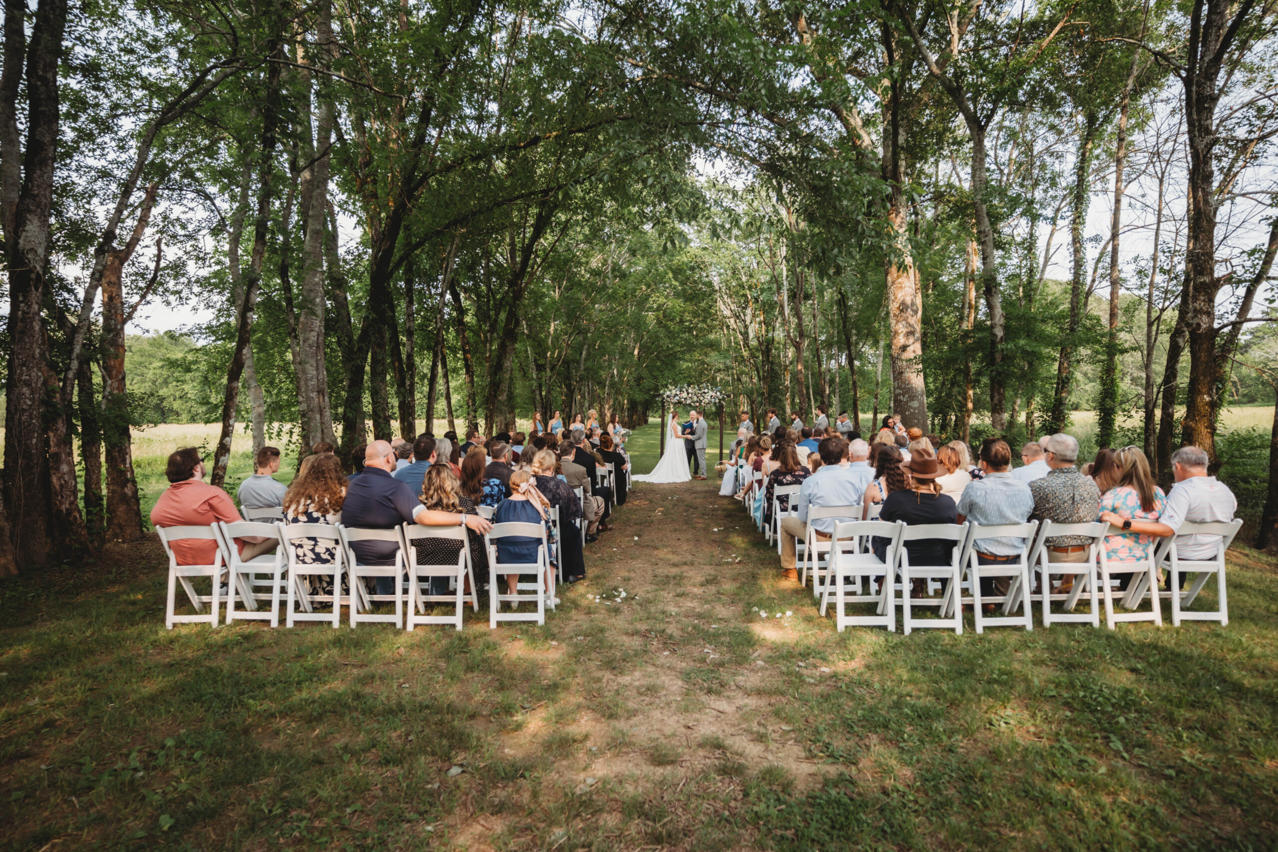 Guests fill the aisle as Anna & Jaden stand under a floral arch in the Tunnel of Love at Covey Creek.