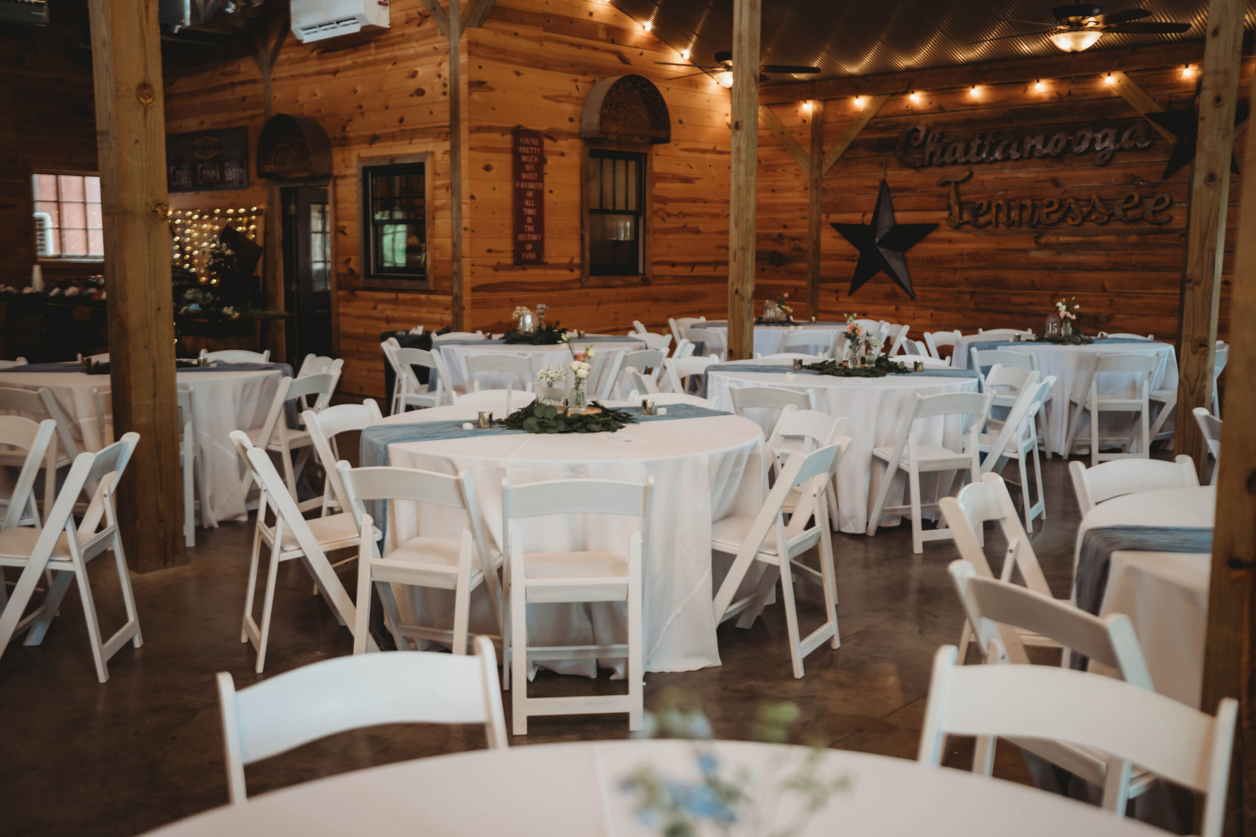 Round tables with white linens, blue runners, and eucalyptus sit ready in the barn for Anna & Jaden at Covey Creek.
