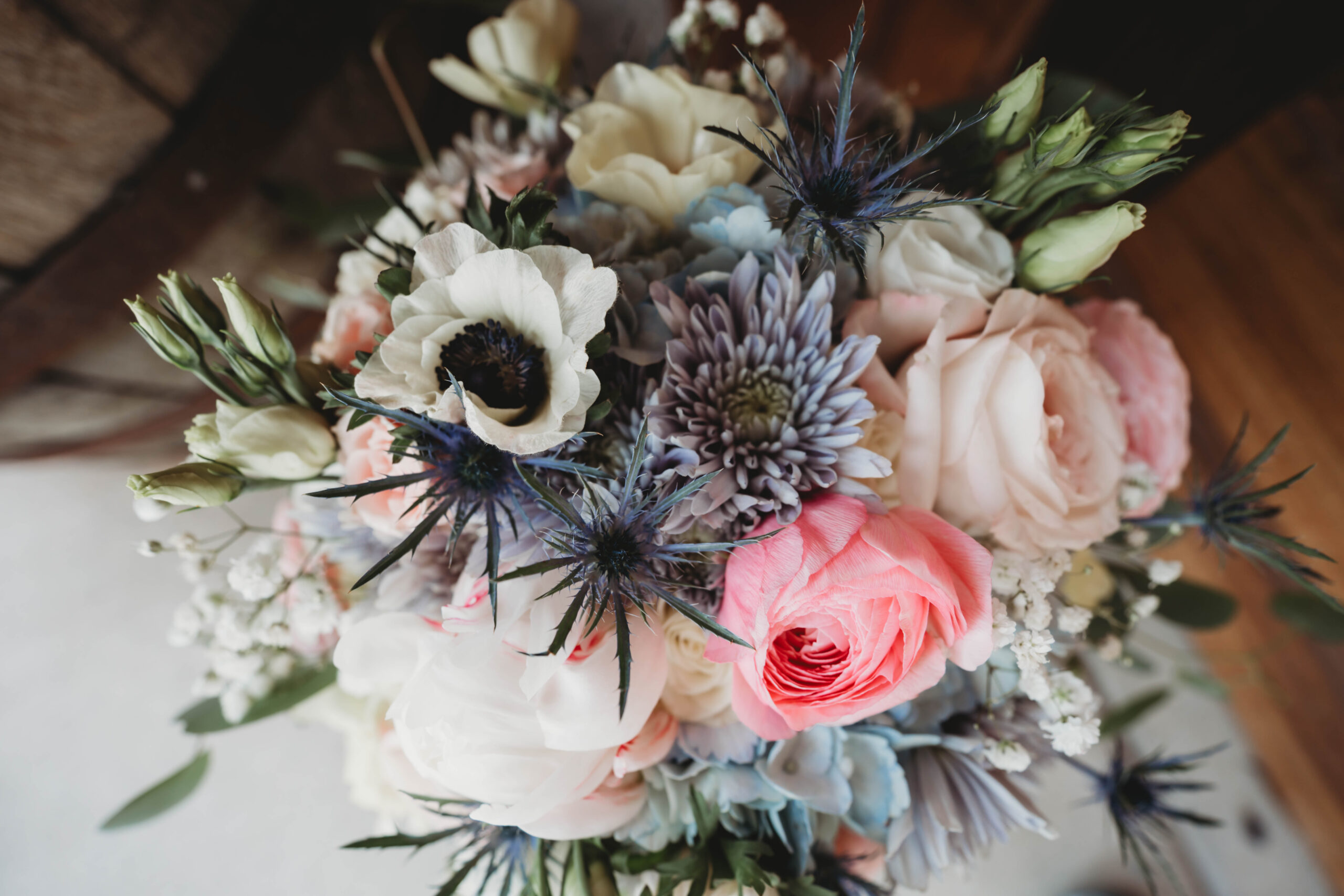 Close-up of Anna & Jaden's bouquet with pink roses, white anemones, and blue thistles at Covey Creek.