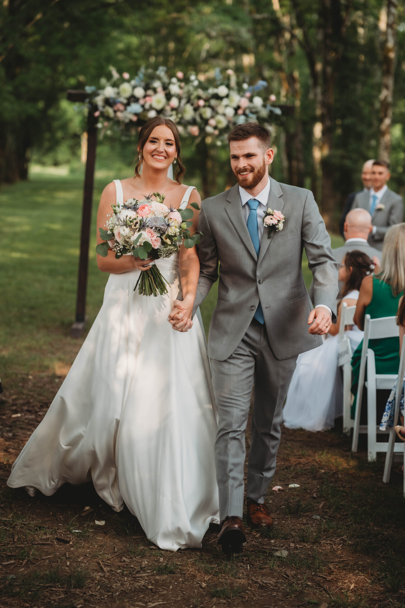 Anna & Jaden smile walking hand-in-hand past guests after their wooded ceremony at Covey Creek.