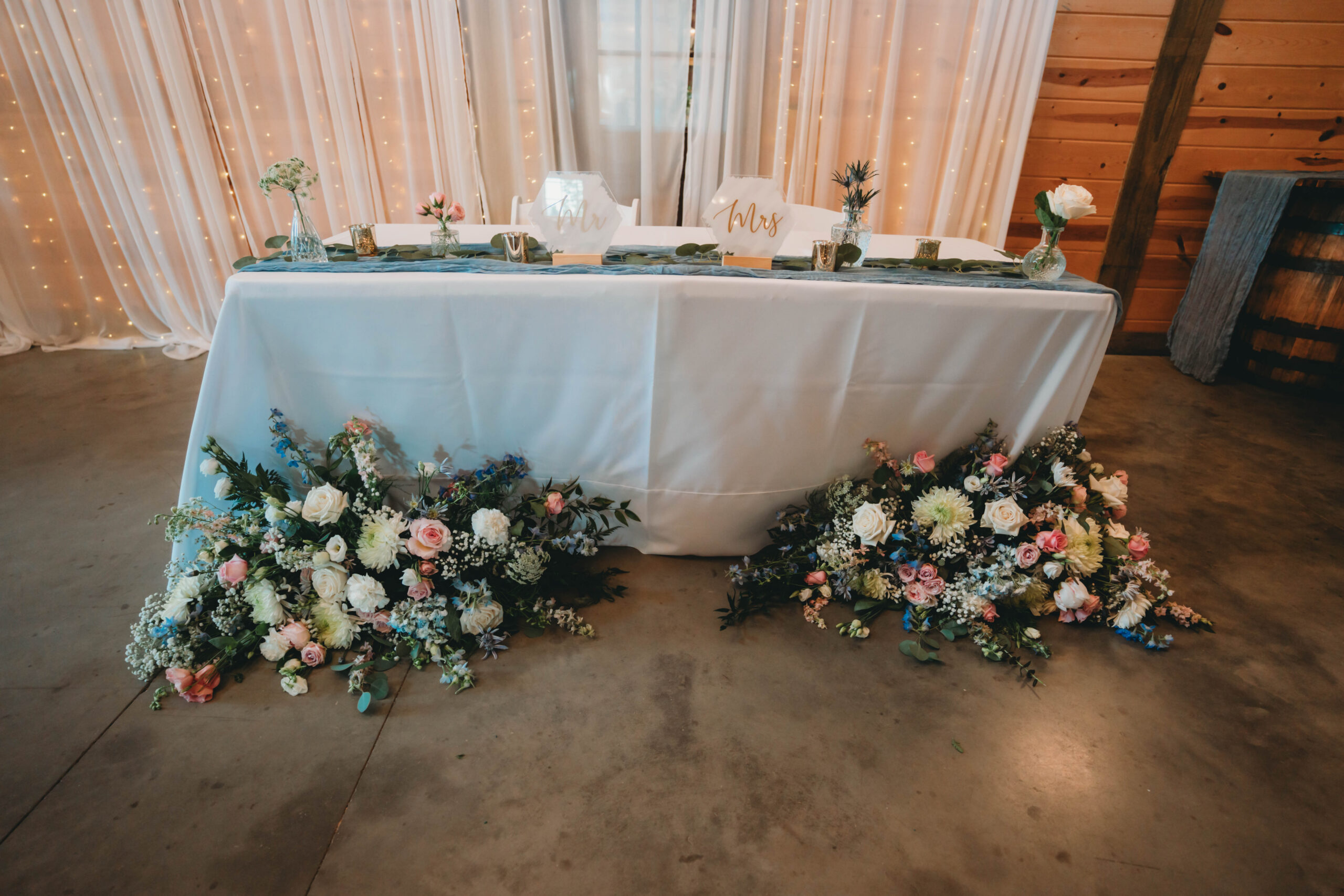 Anna & Jaden's sweetheart table with Mr. and Mrs. signs and floor florals under lights at Covey Creek.