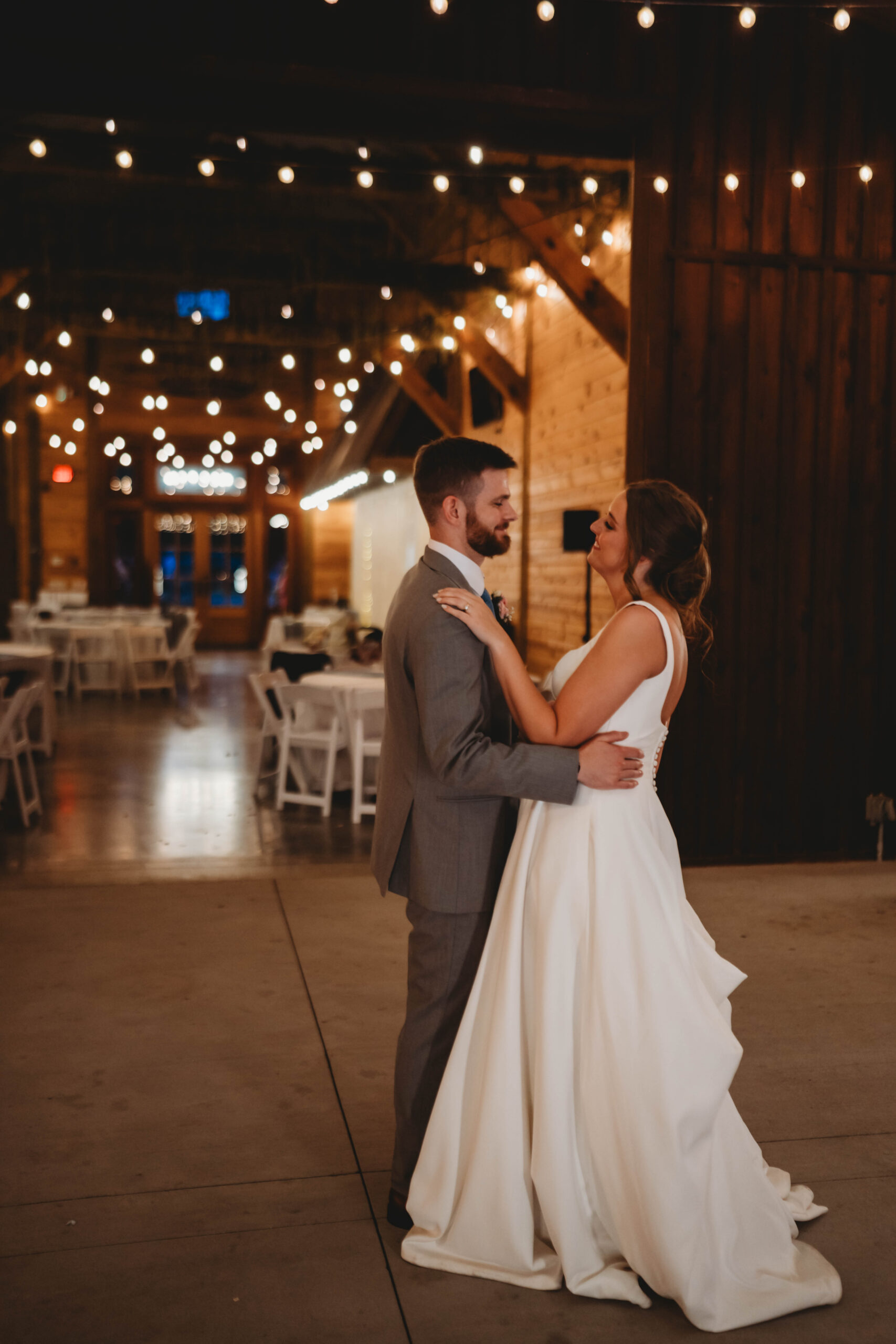 Anna & Jaden smile face-to-face under warm string lights at their barn reception at Covey Creek.