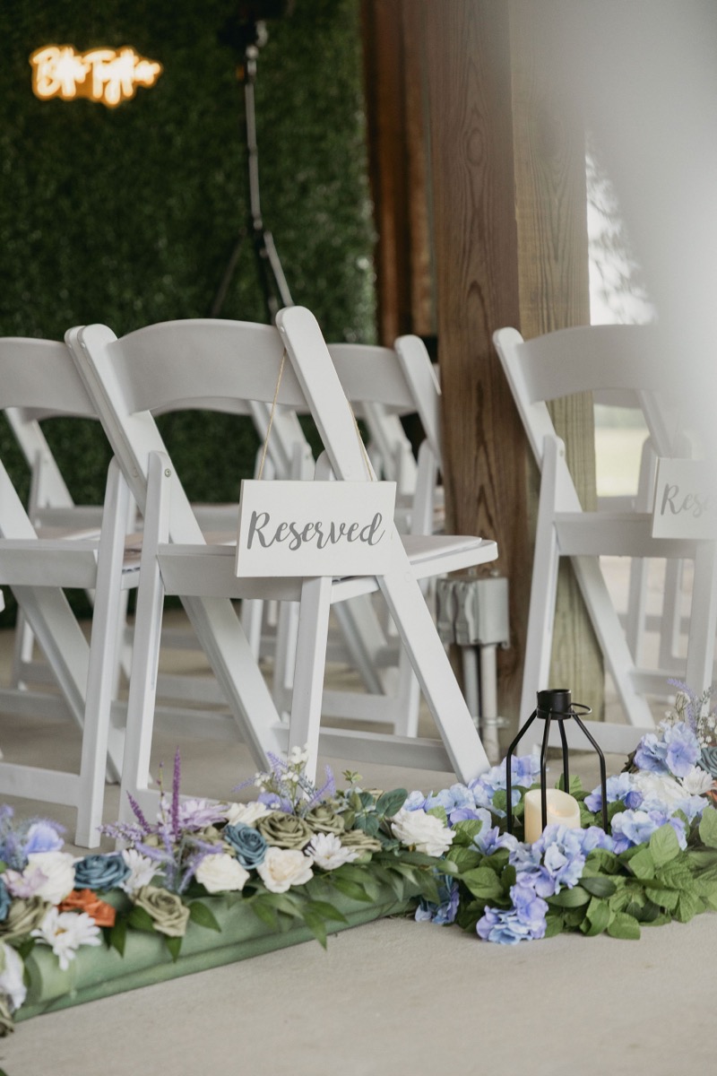 Reserved chair and blue aisle florals with a candle lantern for Brianna & Michael's patio pavilion ceremony at Covey Creek.