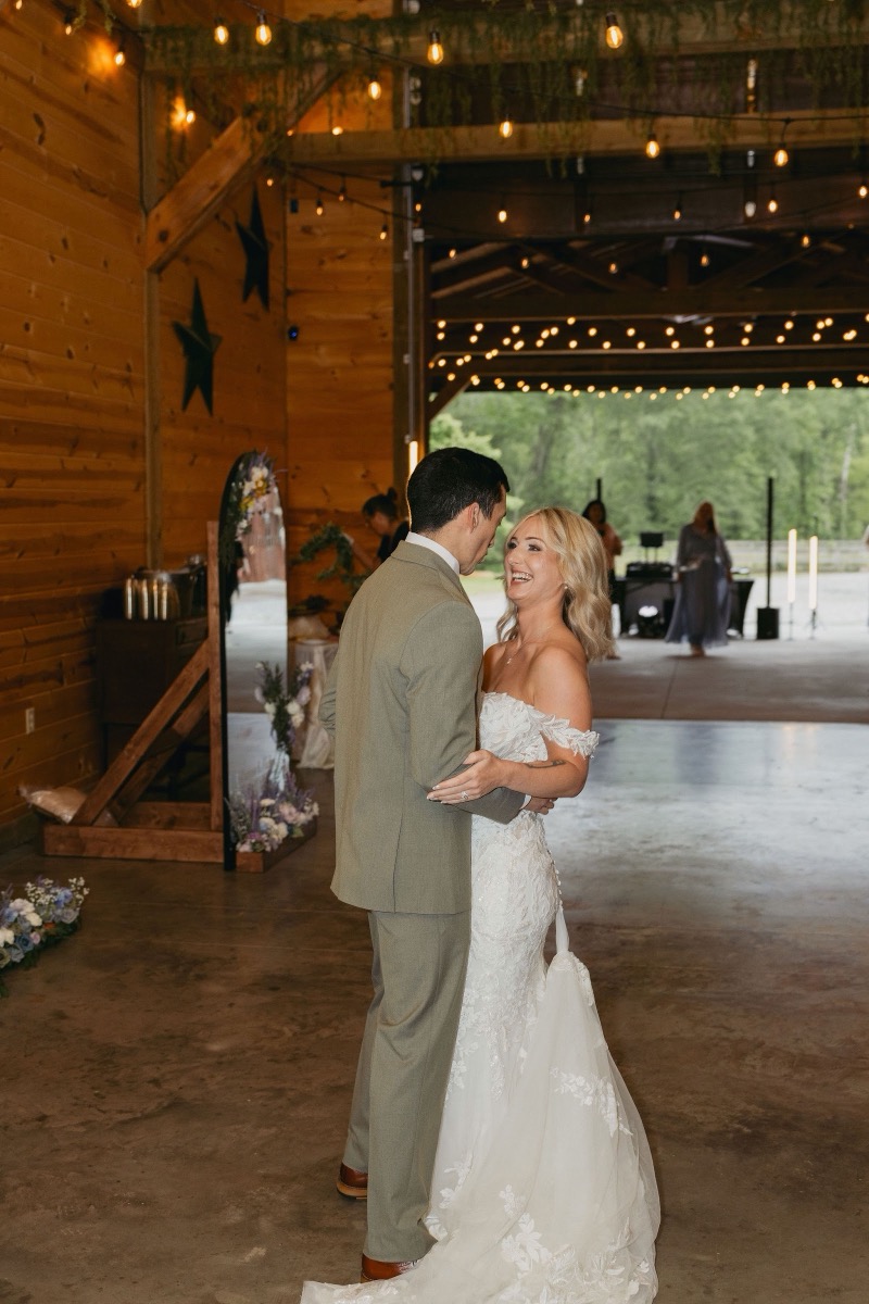 Brianna & Michael dance as she laughs near an arched floral mirror in Covey Creek's string-lit reception barn.