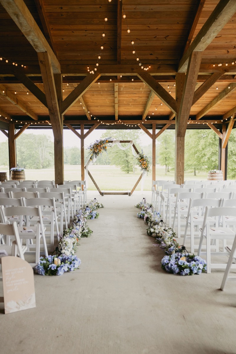 Hexagonal sunflower arbor and blue-hydrangea aisle with lanterns set for Brianna & Michael in Covey Creek's patio pavilion.