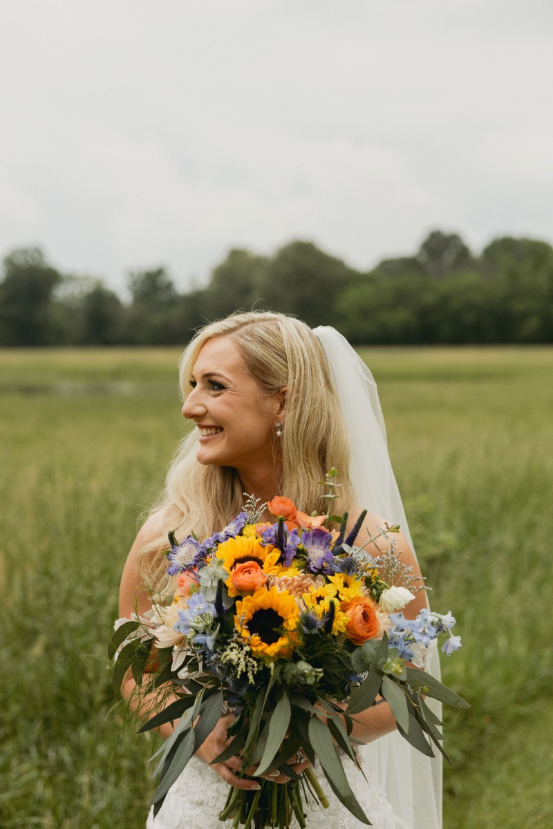Brianna smiles in profile with sunflower and blue-thistle bouquet and veil—Brianna & Michael portraits at Covey Creek.