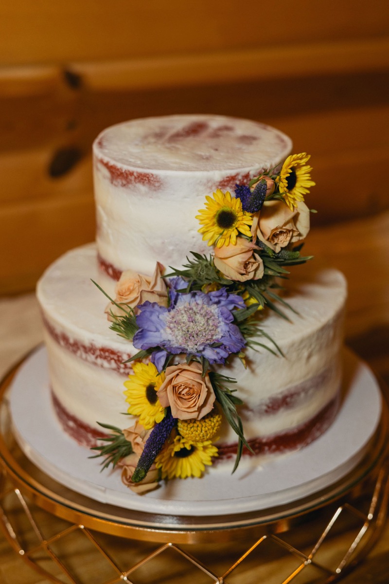 Semi-naked two-tier cake with sunflowers and peach roses on a gold stand for Brianna & Michael at Covey Creek.